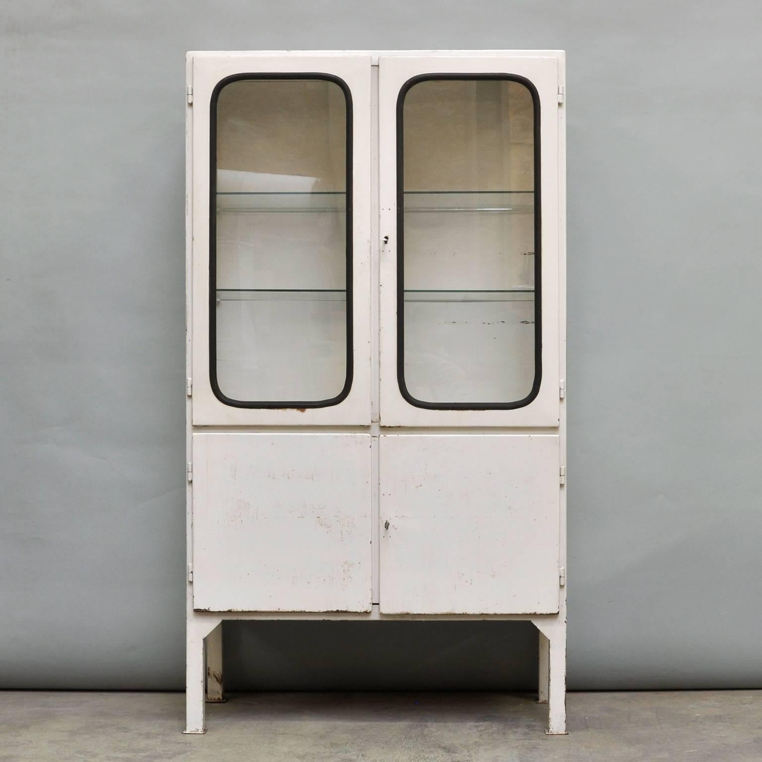 This medicine cabinet was designed in the 1970s and was produced circa 1975 in Hungary. It is made from iron and glass, and the glass is held by a black rubber strip. The cabinet features two adjustable glass shelves and functioning locks. The