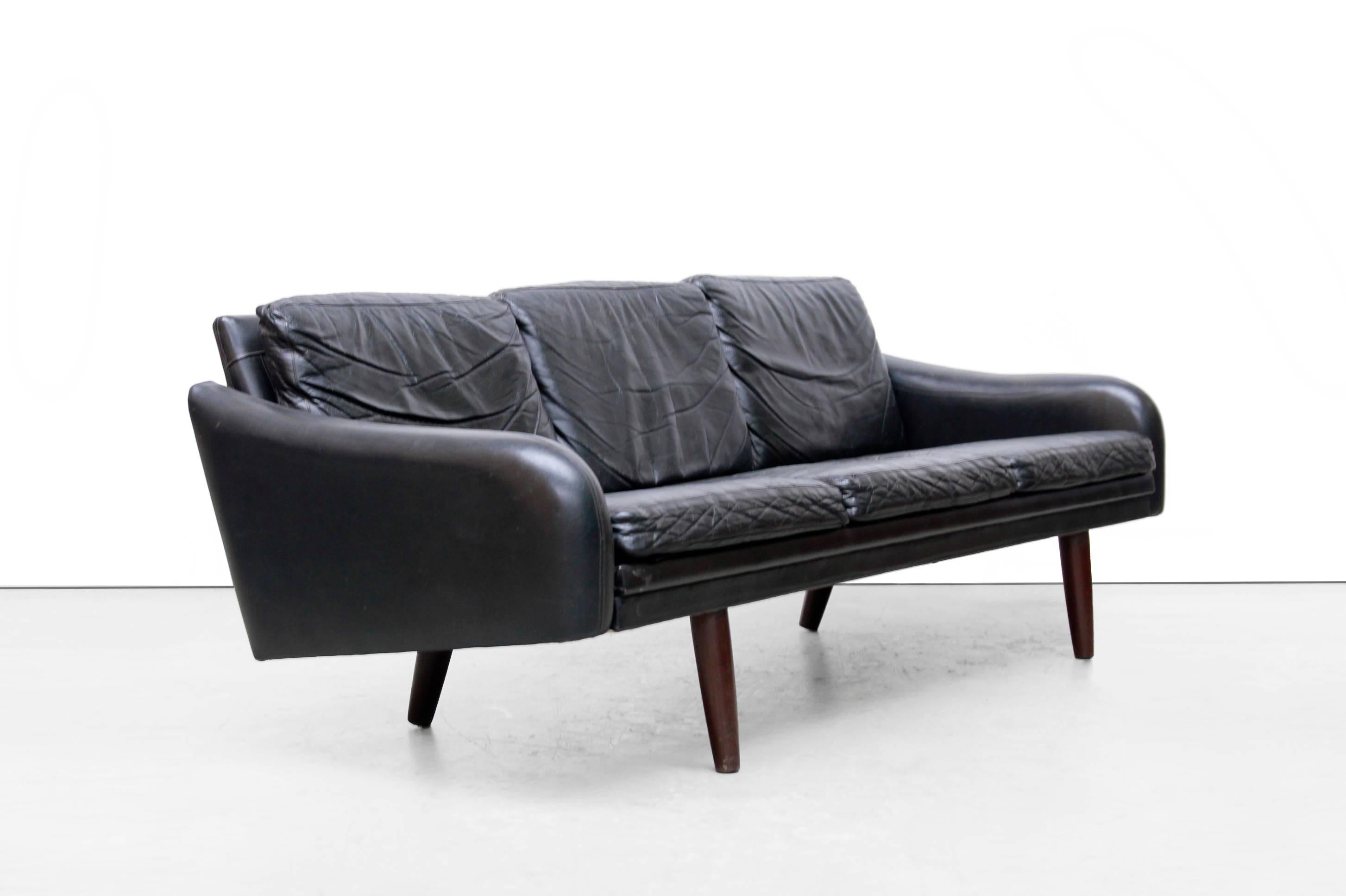 Black leather three-seat sofa from Danish furniture manufacturer. This sofa offers space for three people and is made of thick black leather with conical wooden legs. The armrests have a beautiful design, the high legs creates visual space, while it