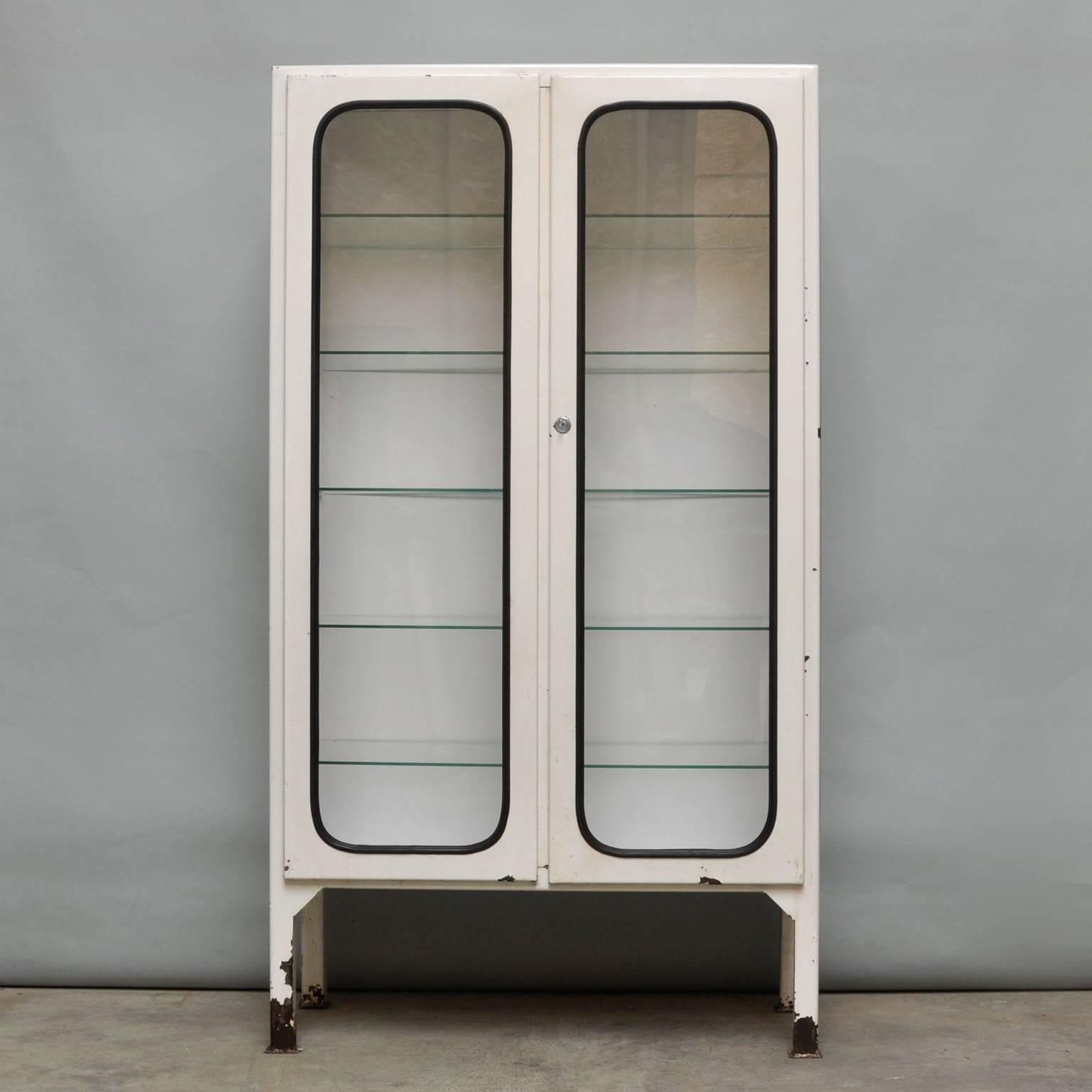 This former medical cabinet was designed in the 1970s and produced, circa 1975 in Hungary. It is made of iron and glass. The glass is secured by a black rubber strip. The cabinet comes with five new adjustable glass shelves and a functioning lock.