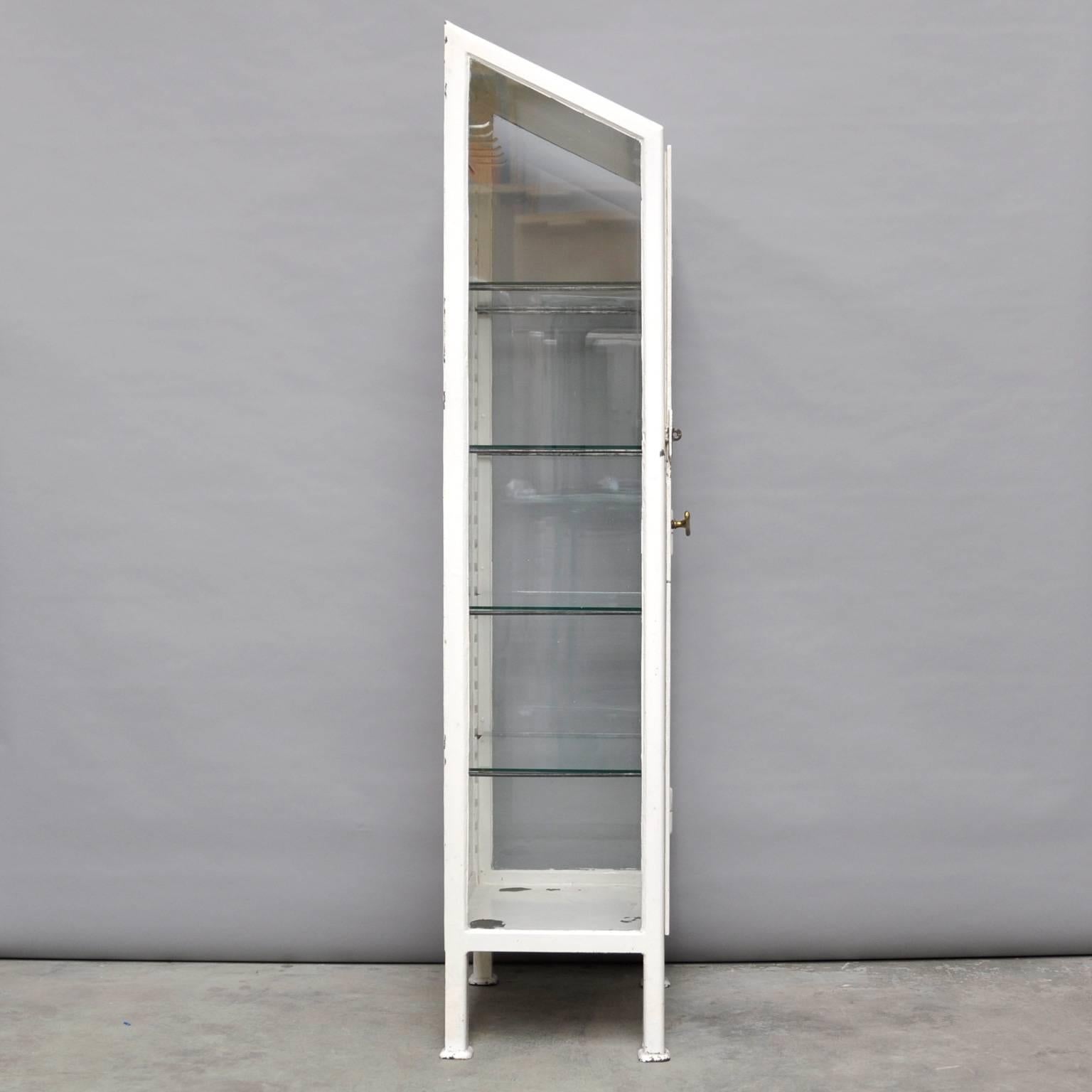 This vintage cabinet was produced in Hungary during the 1930s. The cabinet is made of thick steel and comes with four glass shelves. The glass of the cabinet is antiqued. The inside of the cabinet features six clothing hooks.