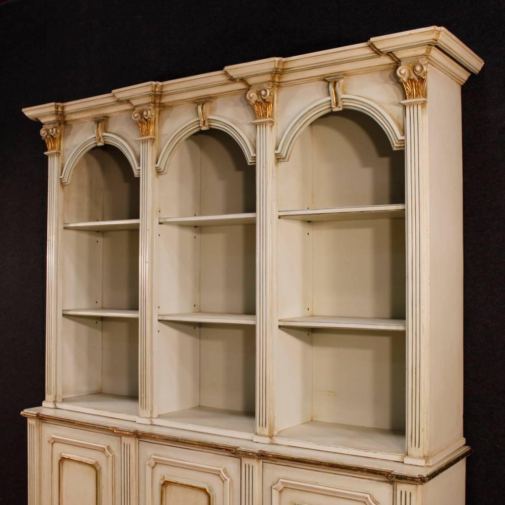 Italian 20th century bookcase. Furniture in carved and lacquered wood decorated with golden capitals of fabulous decoration. Double body bookcase with three doors at the bottom. Upper body complete with six shelves ideal to expose collections of