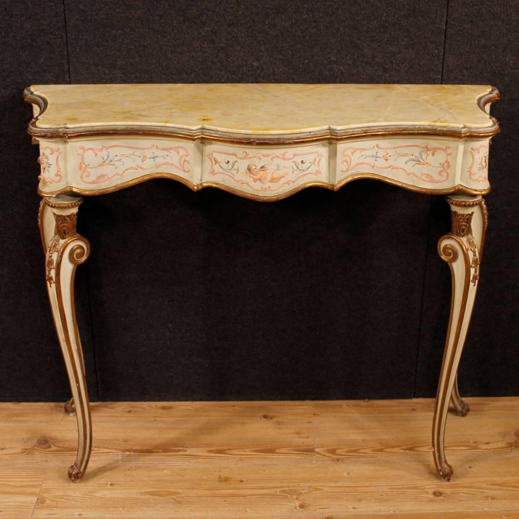 Italian console table of the mid-20th century. Furniture in richly carved, lacquered, gilded and hand painted wood with floral decorations and central little angel, of great quality. Console of excellent proportion, it can be easily inserted in