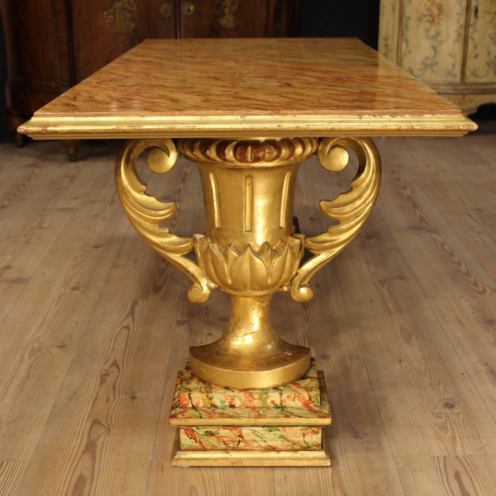 Gilded, lacquered and painted by hand coffee table of the 20th century. Furniture of good stability supported by two special cupped legs made by carved and gilded wood. Lacquered faux marble top, of great decoration. Decorations in wrought iron on