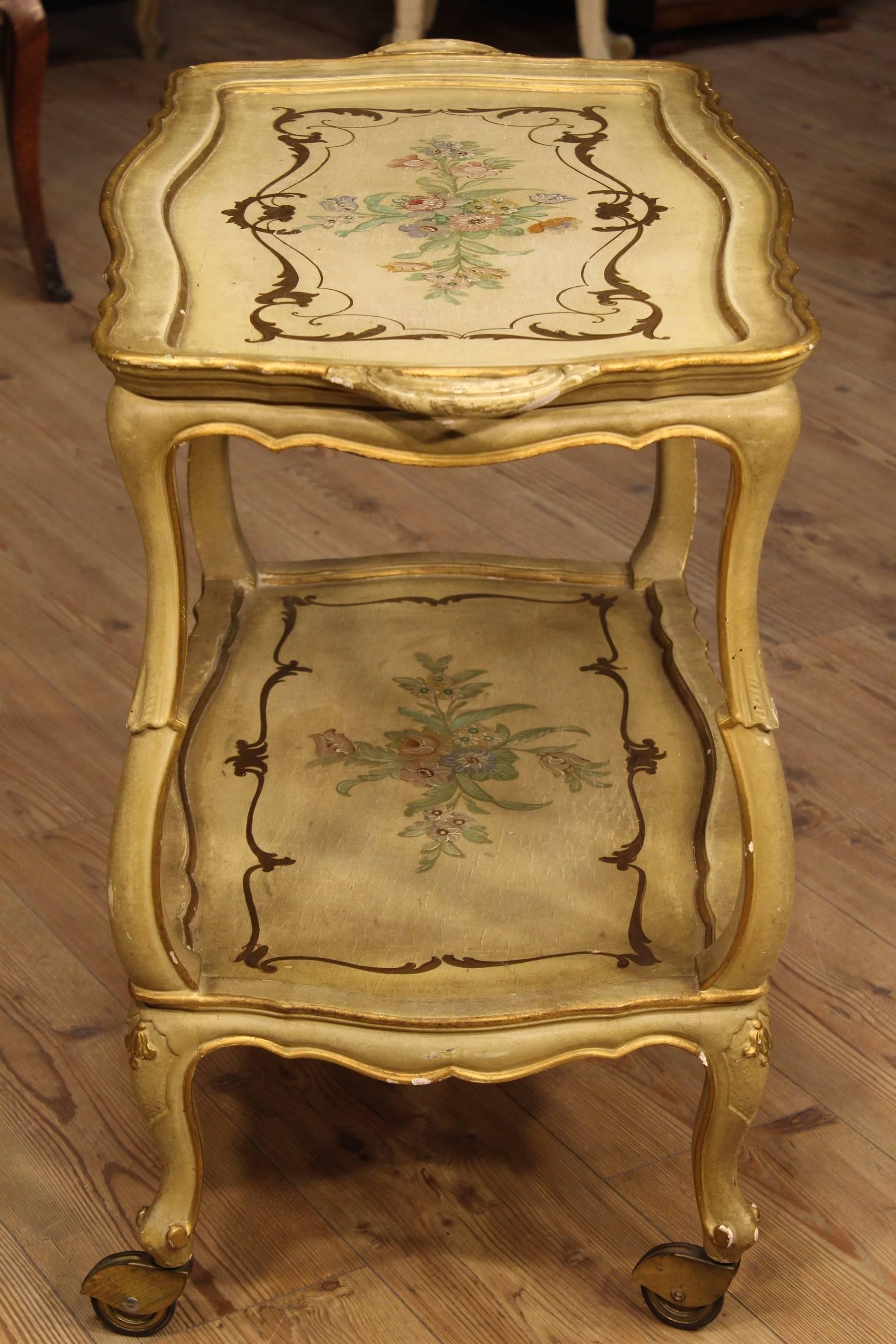 Venetian coffee table made by finely carved, lacquered, gilded and hand-painted with floral motifs wood. Cart furniture with two shelves provided with four wheels for easier movement and use. Side table of the second half of the 20th century, ideal