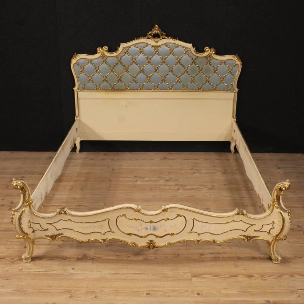 Scenic Italian double bed of the mid-20th century. Furniture in ornately carved, lacquered, gilded and hand-painted wood with floral decorations, of great taste. Bed of fabulous decor and great impact decorated with fabric headboard, which presents