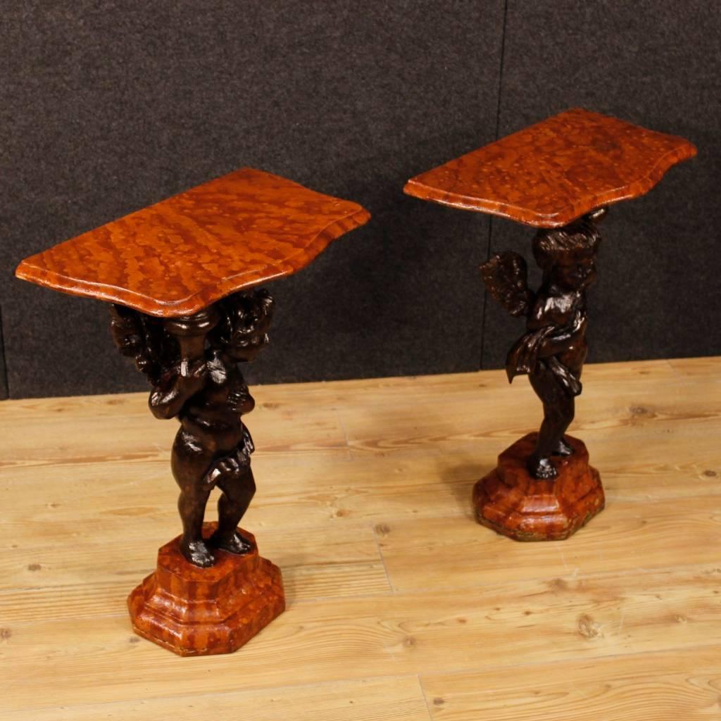 Pair of Italian side tables from the 20th century. Carved and lacquered wooden furniture, of nice decor. Basement and top floor in lacquered faux marble wood, central body wood tinted with little angels with wings sculptures. Wall-hung tables of