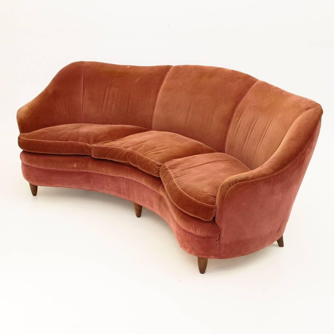 This curved sofa was produced in Italy in the 1950s. The frame is made from wood and the seats are upholstered in velvet. The feet are conical, there are three seats.