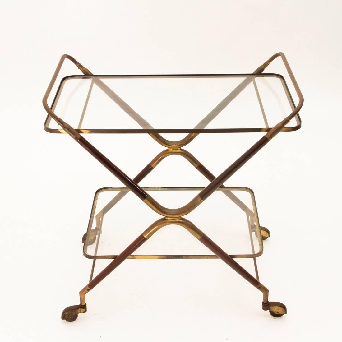 A lunch trolley designed by Cesare Lacca during the 1950s, featuring a double C-structure in inverted brass and lacquered wood, two shelves with an edge in brass, a glass top, brass details and rubber wheels.
