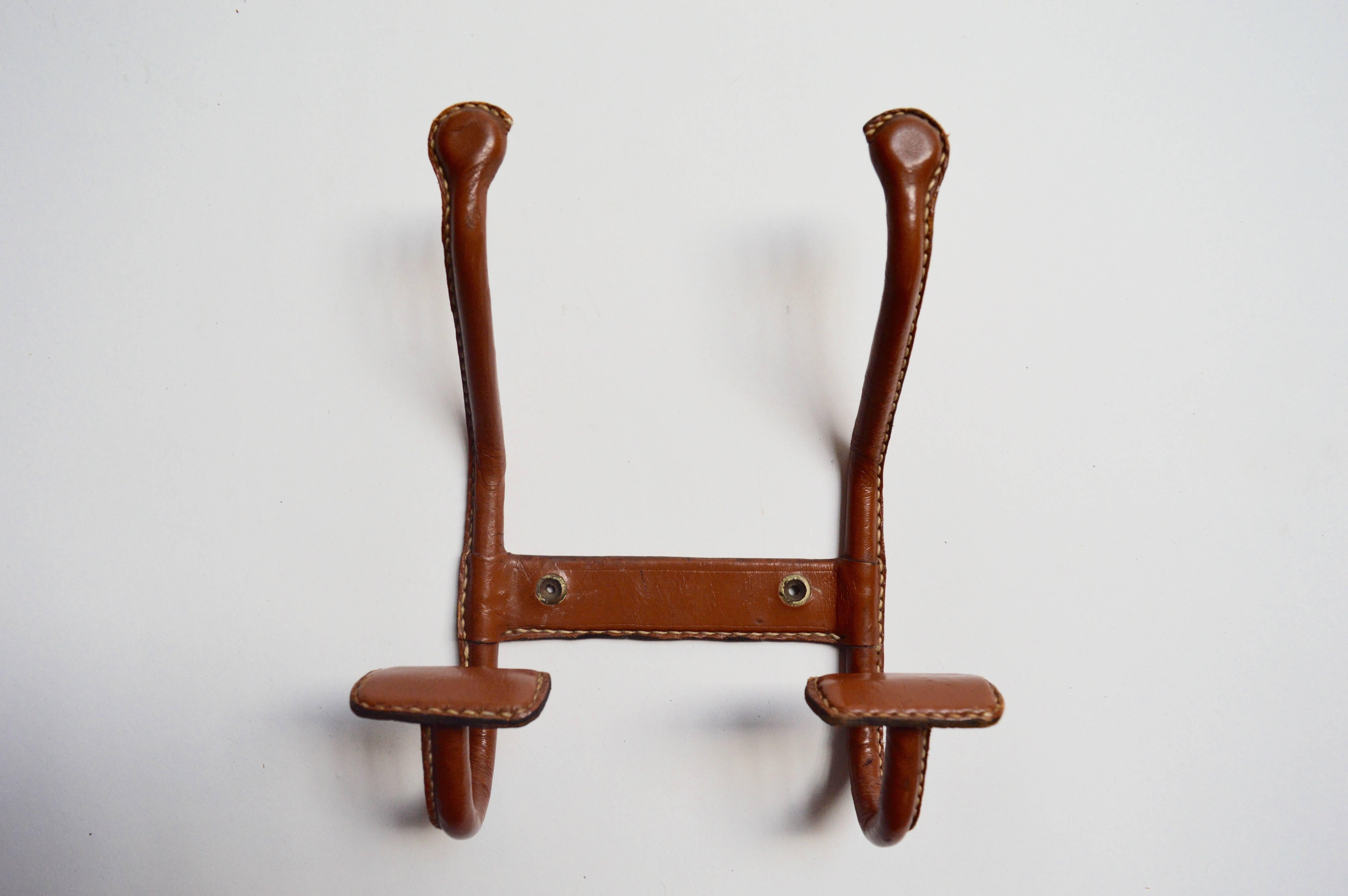 Handsome coat hook by French designer Jacques Adnet. Saddle leather has beautiful patina and is in excellent vintage condition. Signature contrast stitching throughout. Hook is in the figure of an 