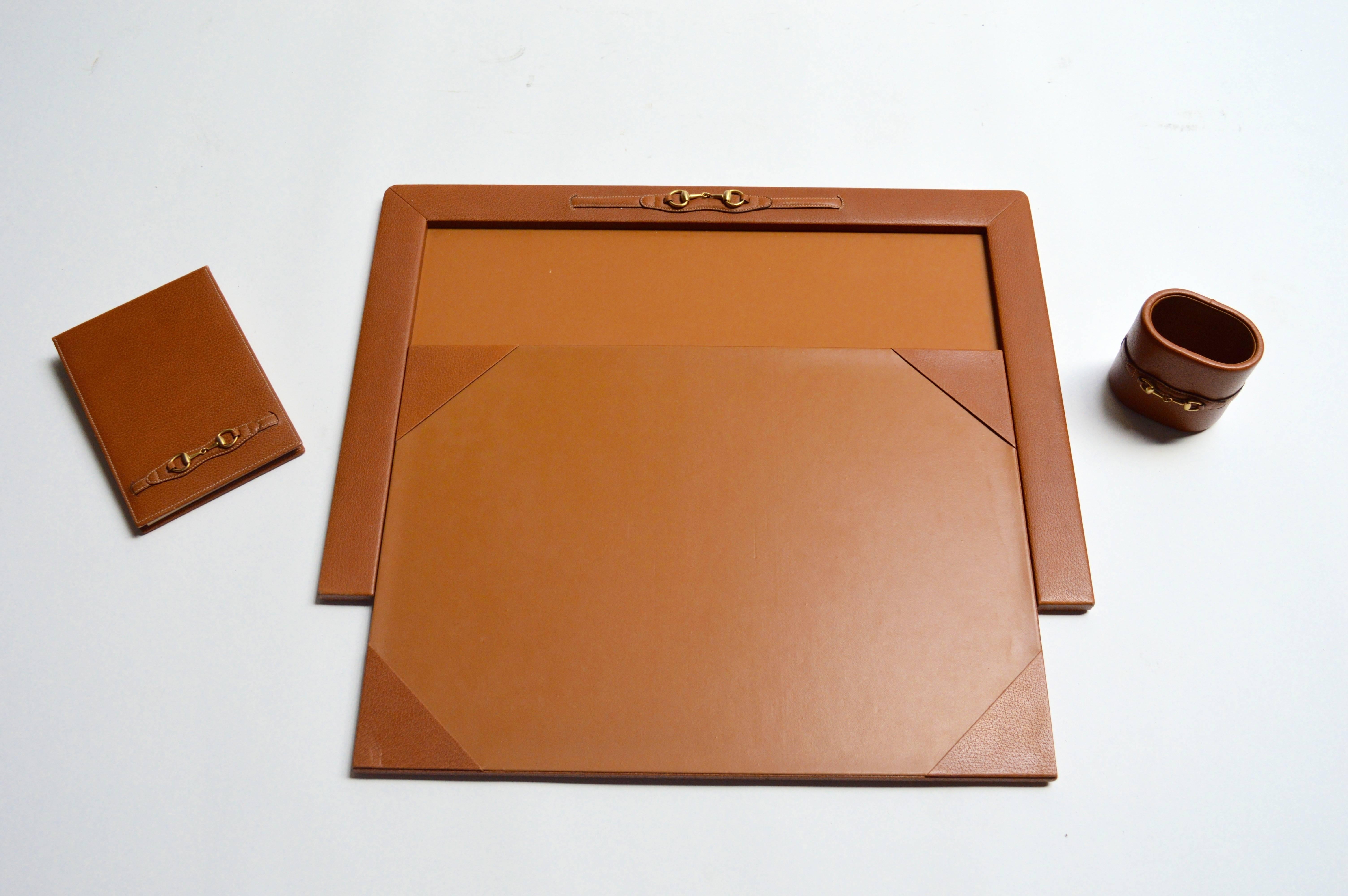 Gorgeous Gucci desk set in saddle leather with brass stirrup hardware. Set features a large desk pad, pen cup and note pad. Original Gucci notepad paper inside. Set is in excellent vintage condition.