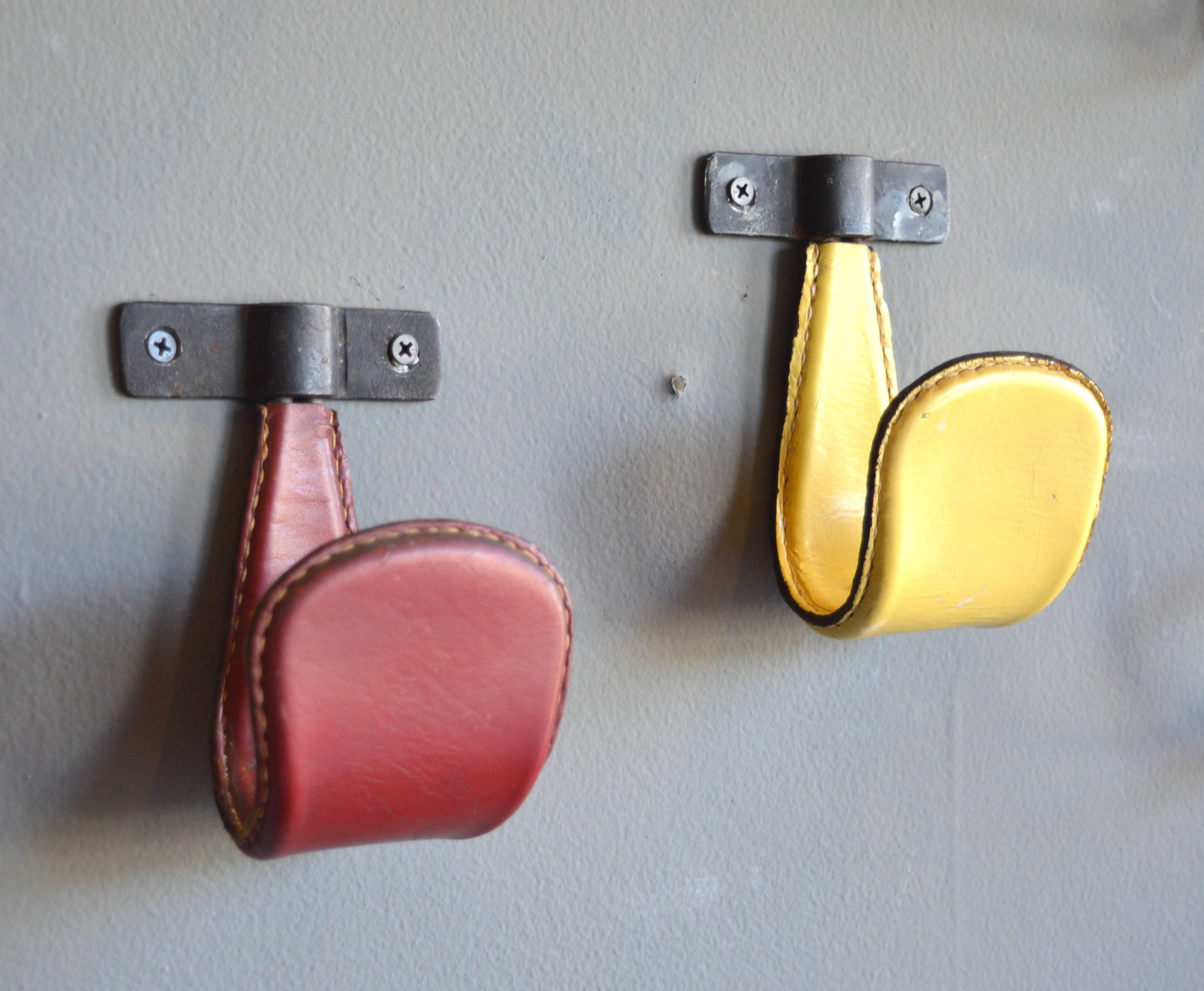 Vintage leather and iron tongue hooks by French designer Jacques Adnet. One red and one yellow. Excellent vintage condition. Priced individually.