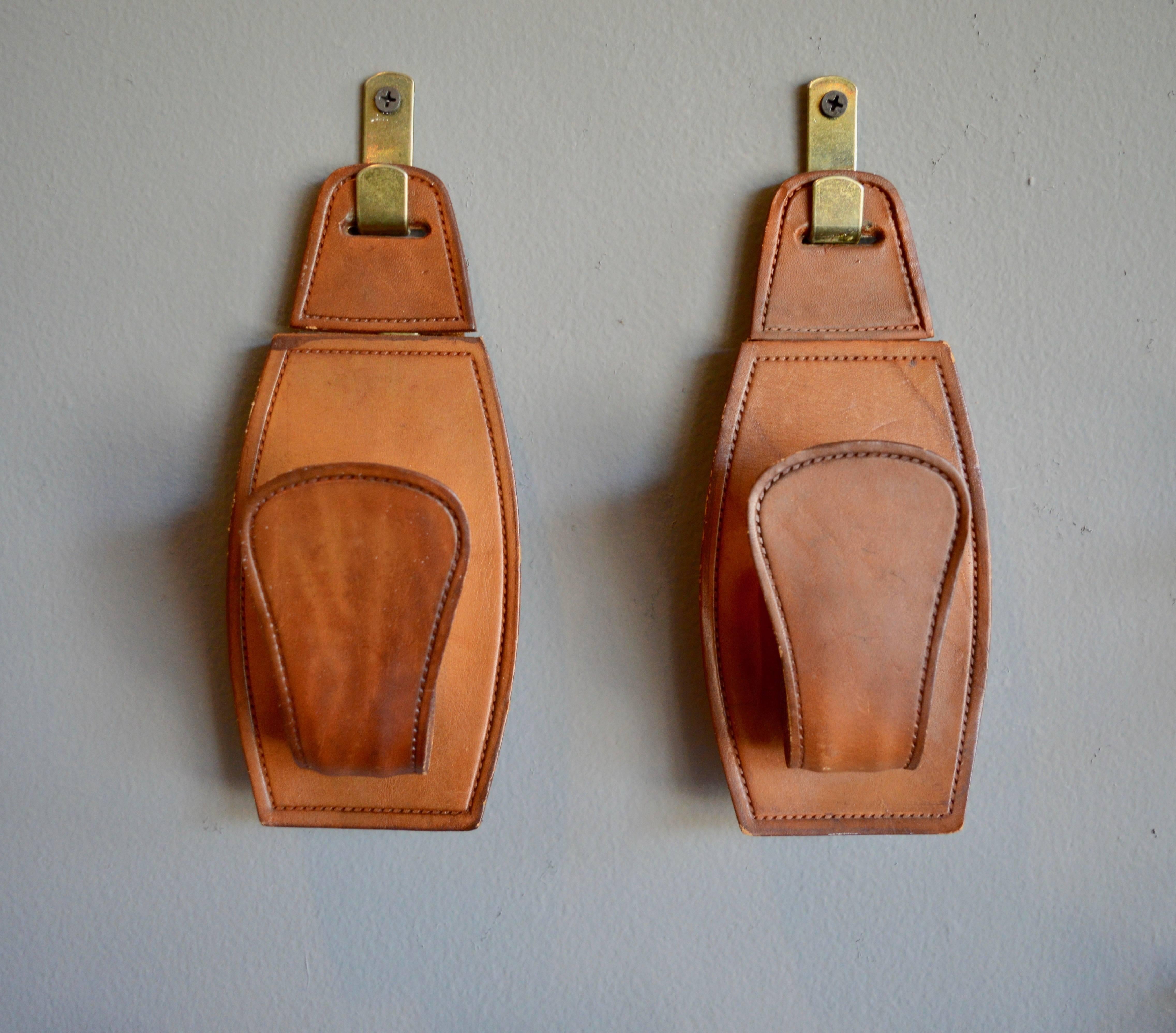French saddle leather hooks in the style of Jacques Adnet. Beautiful saddle leather with rich patina. Hooks have brass clips to hang them. Clips can be removed and hooks can be hung with a center screw. Three hooks available. Priced individually.