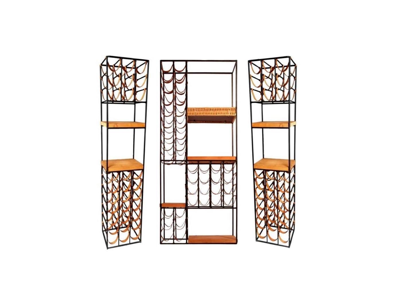 Fantastic set of three vintage Arthur Umanoff wine racks. Two matching wine racks flanking a larger centre rack. Holds 100 bottles in the leather slings. Seven additional wood shelves for objects, books or more bottles. One large rattan trimmed