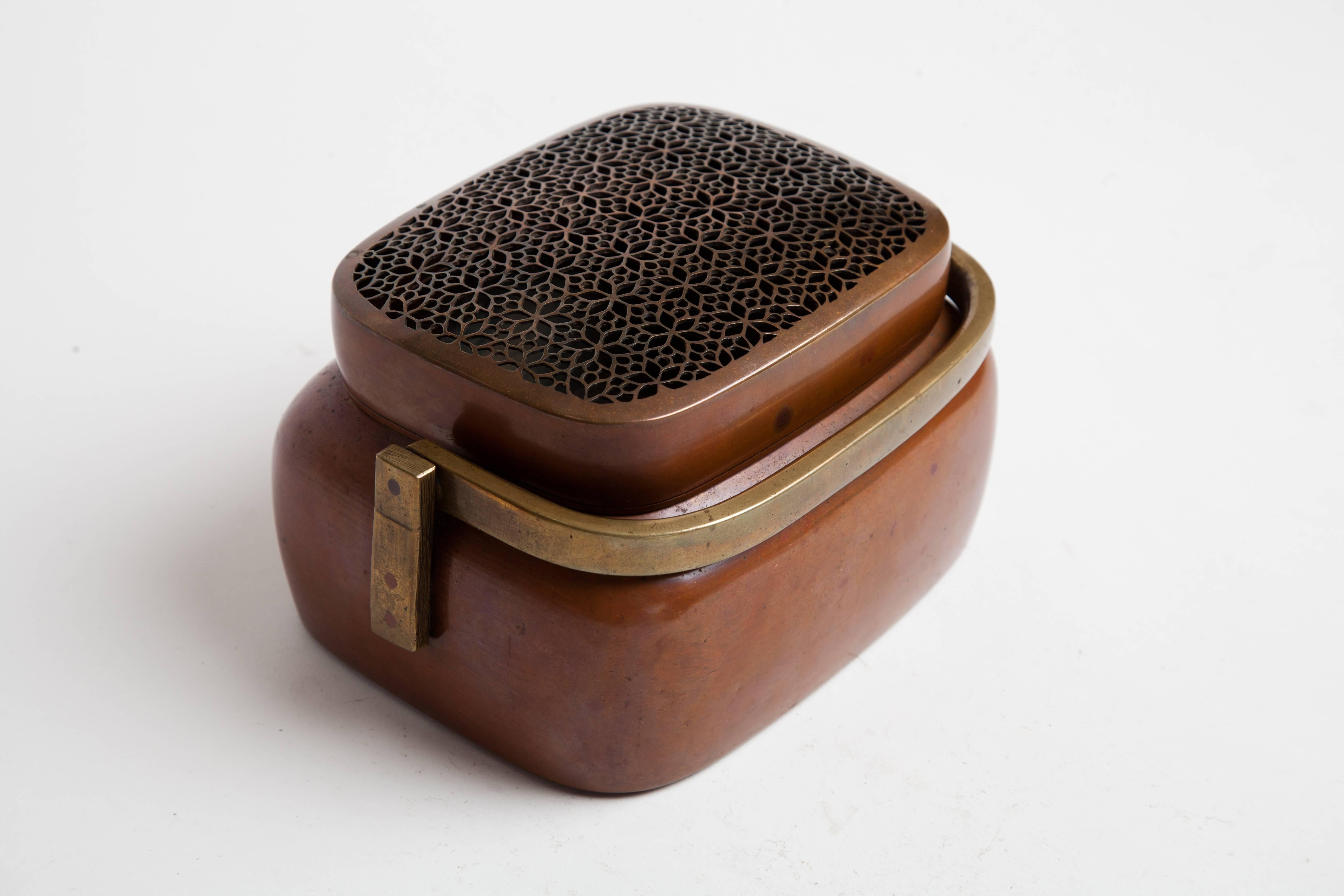 Antique Japanese hand warmer in rectilinear form with hinged handle of cast copper secured to mounts on opposing ends of body with bronze rivets. Hammered copper body and lid with floral pierce work decoration.