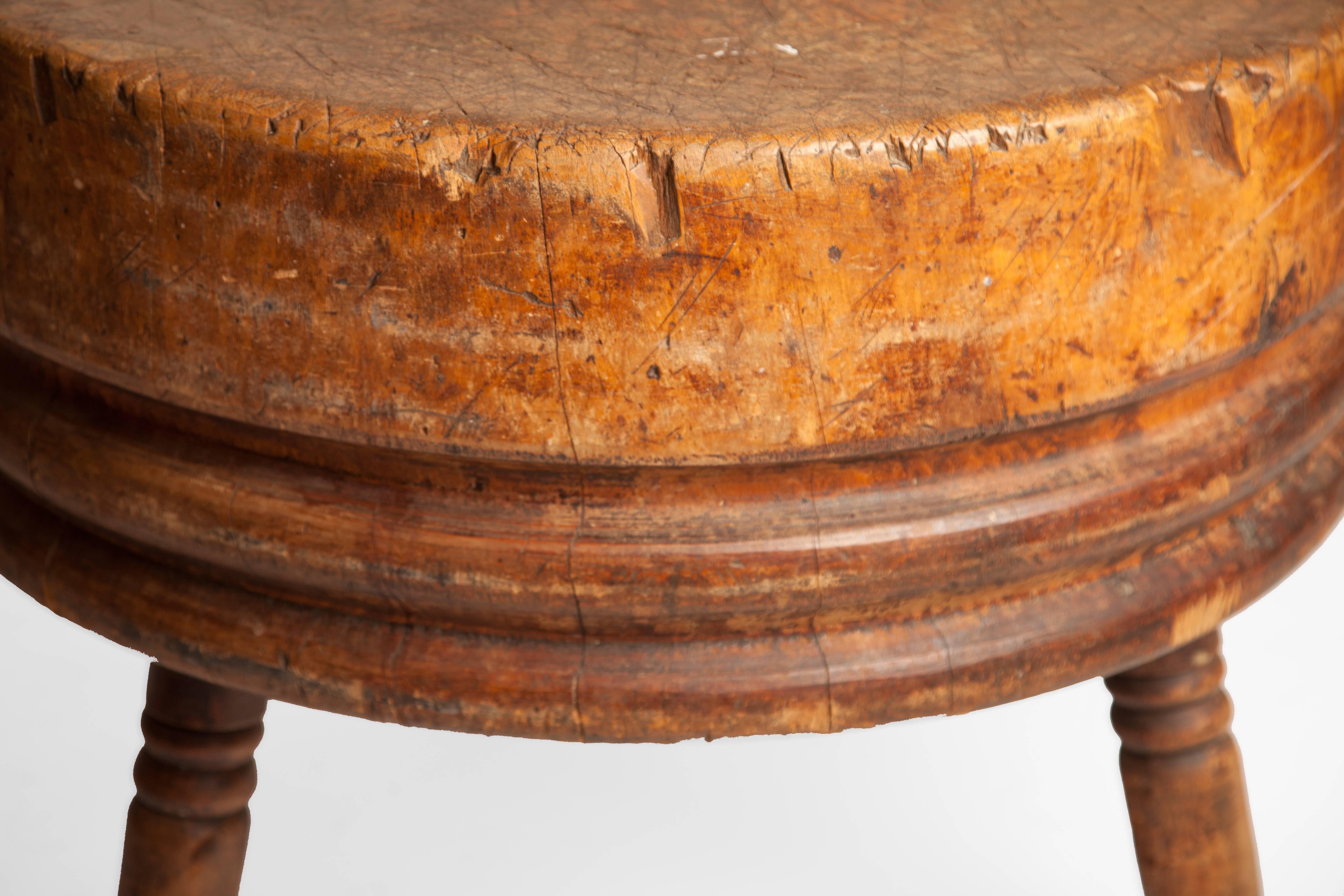 Antique round butcher's block made from a single tree trunk, raised on three turned legs.