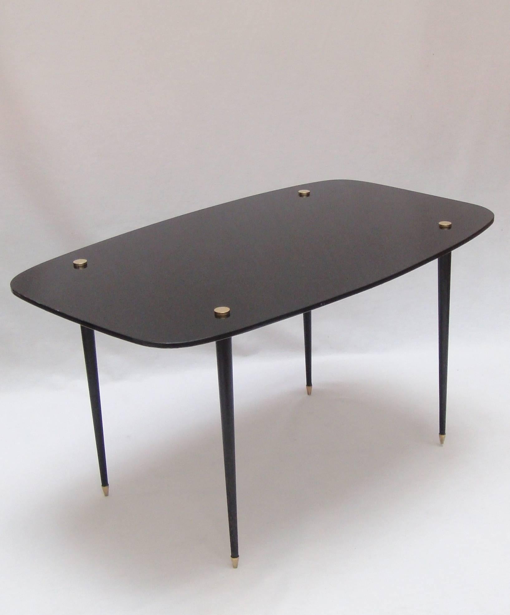A black glass side table with black lacquered metal legs and brass detail.
 