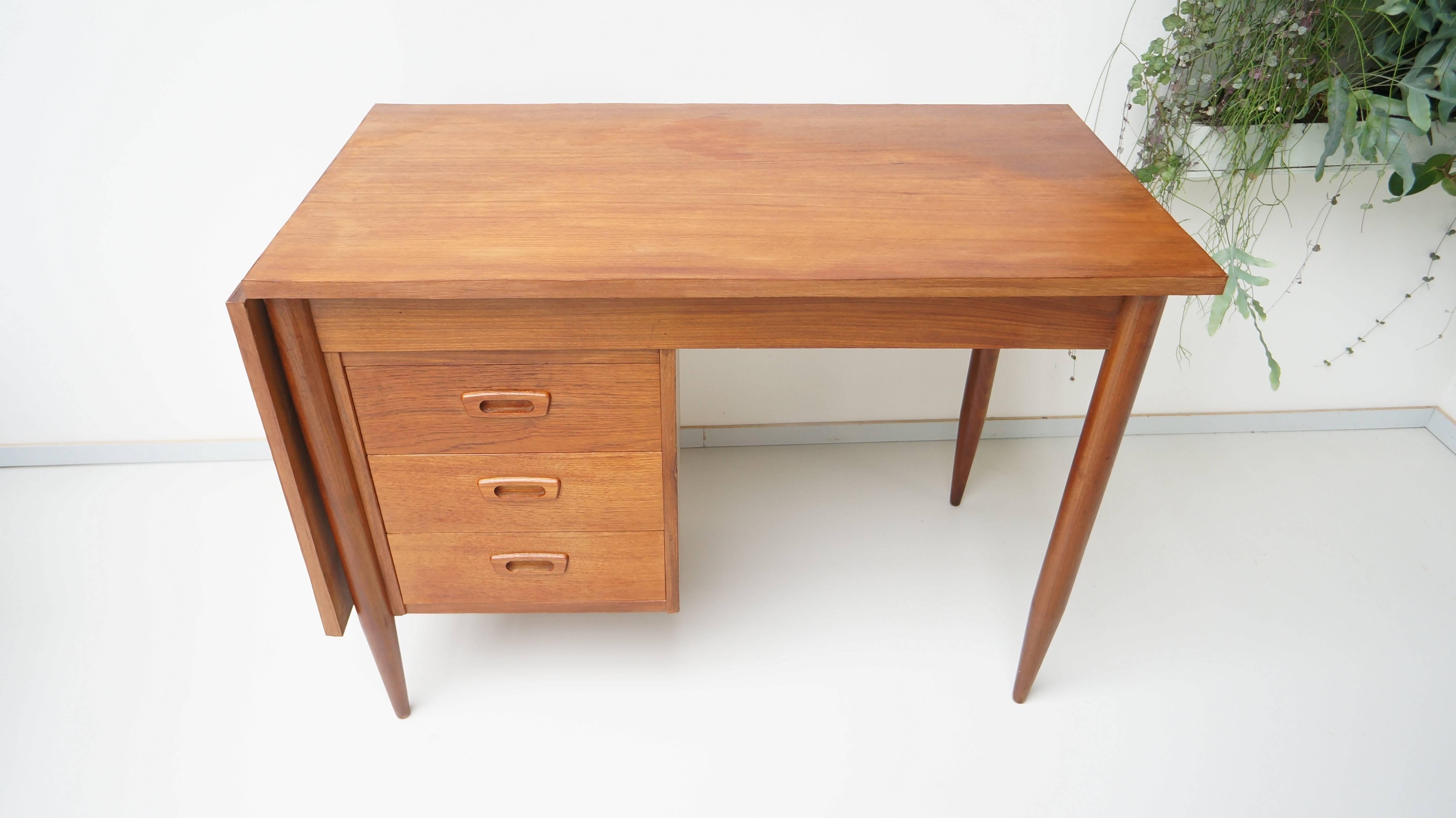 Teak veneer wooden desk from the Danish designer Arne Vodder. The single drawer stack has three drawers with recessed pulls in matching teak wood. The work space has a dropped leaf on the left side. The whole top slides left to support the leaf and