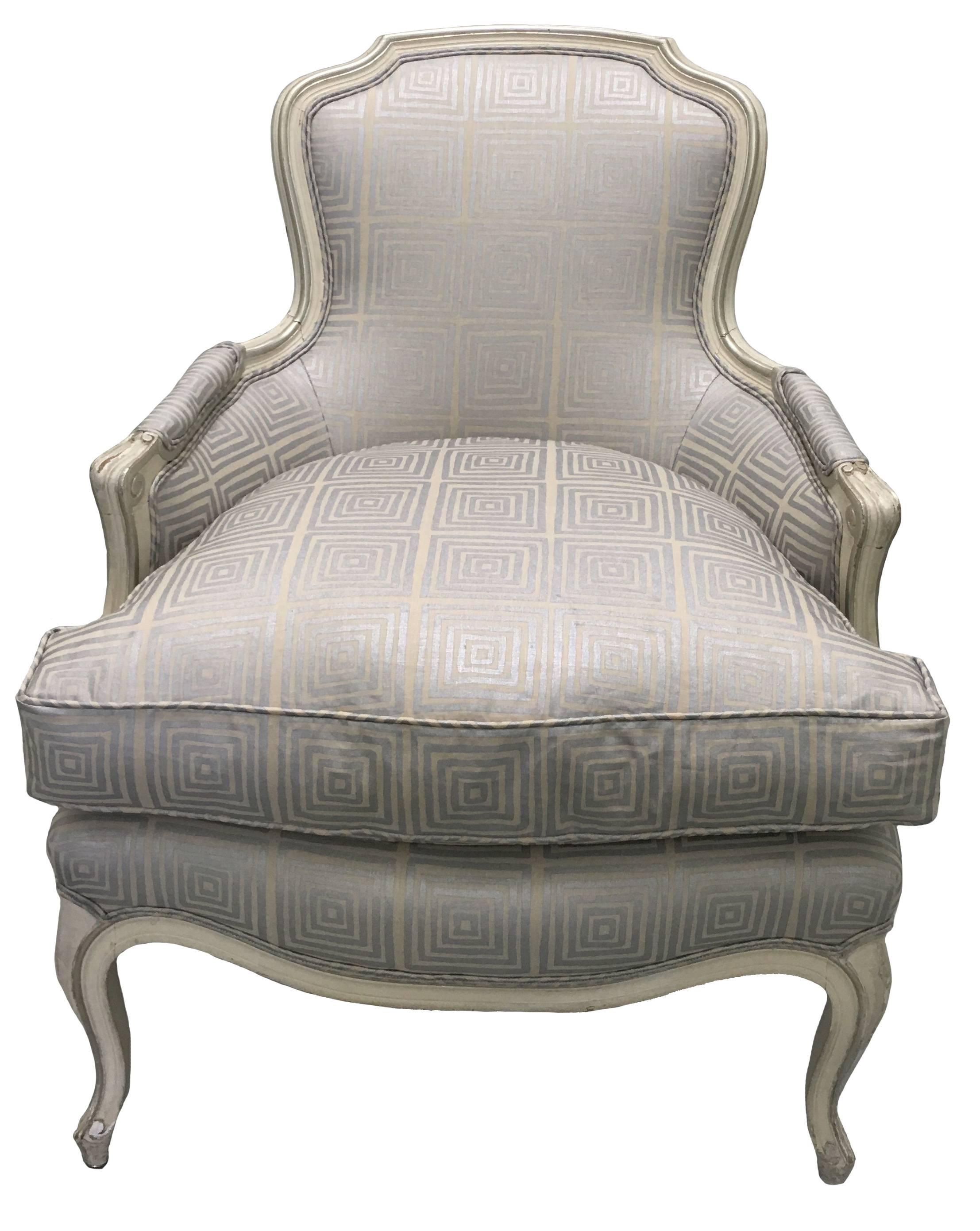 Mid-century Louis XV style bergere chair. Original antique white painted finish with silver accents. Newly upholstered in Quadrille 'Ziggurat' linen in metallic silver/tan. New down filled seat. Arm is 23.5