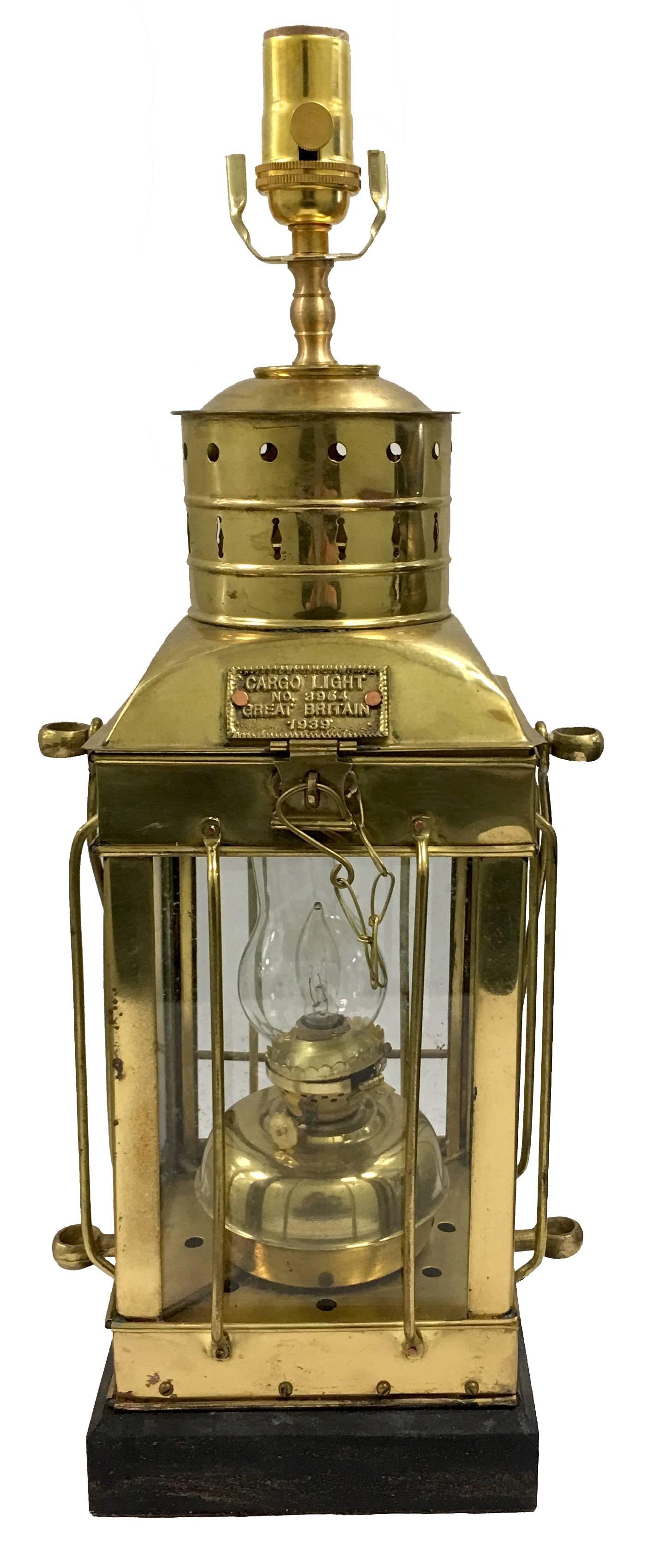 1939 Great Britain brass cargo ship oil lantern previously converted to a table lamp. Black stained wood base. Newly rewired with new fittings/ socket. Takes one standard bulb and one candelabra bulb inside the lantern. Lampshade not included.
