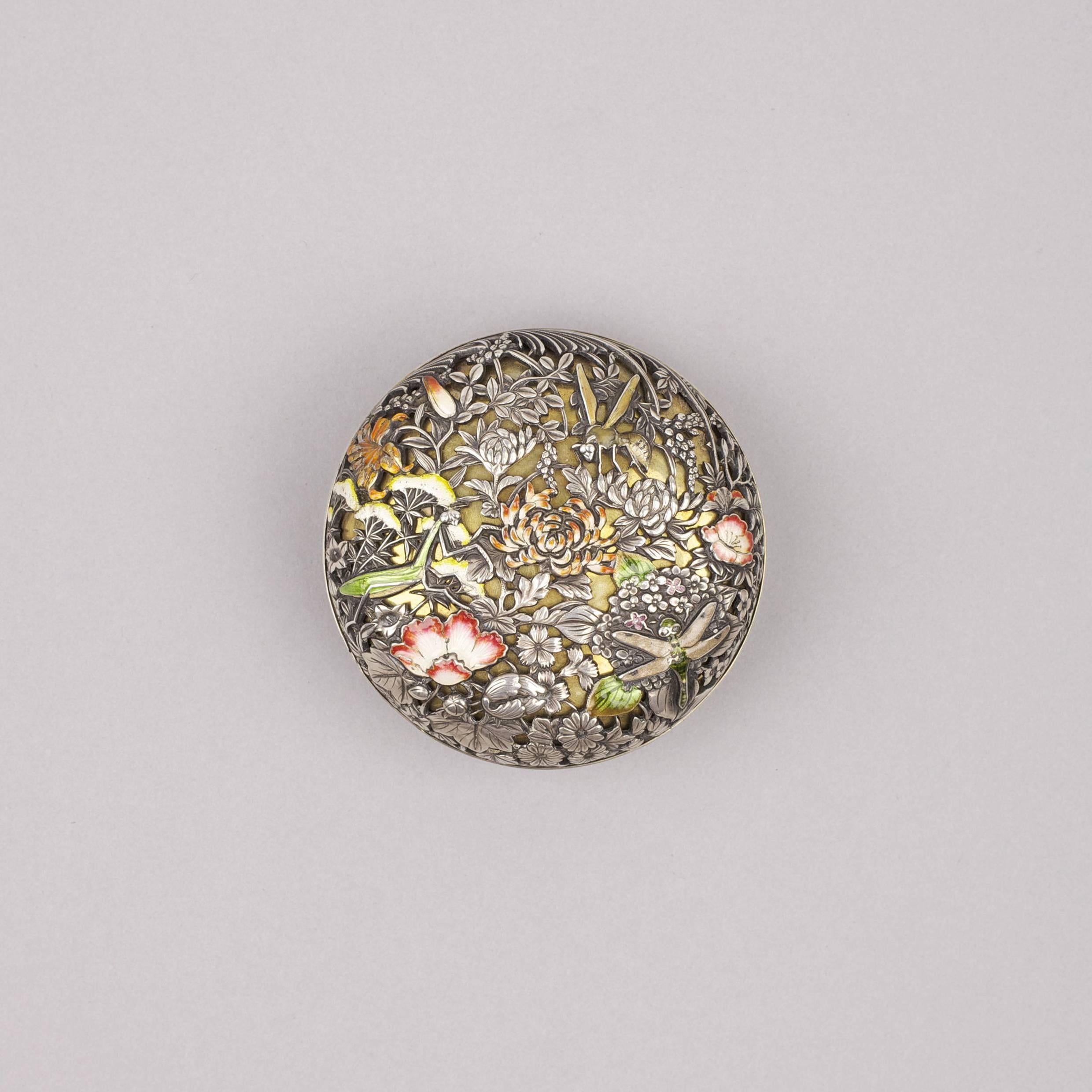 A white-metal and enamel kogo of circular form, decorated in kebori on the base and with a sukashi design of dragonflies and flowers on the cover, the base with two kanji, Shoumin, and a kao-mark.1868 – 1912.