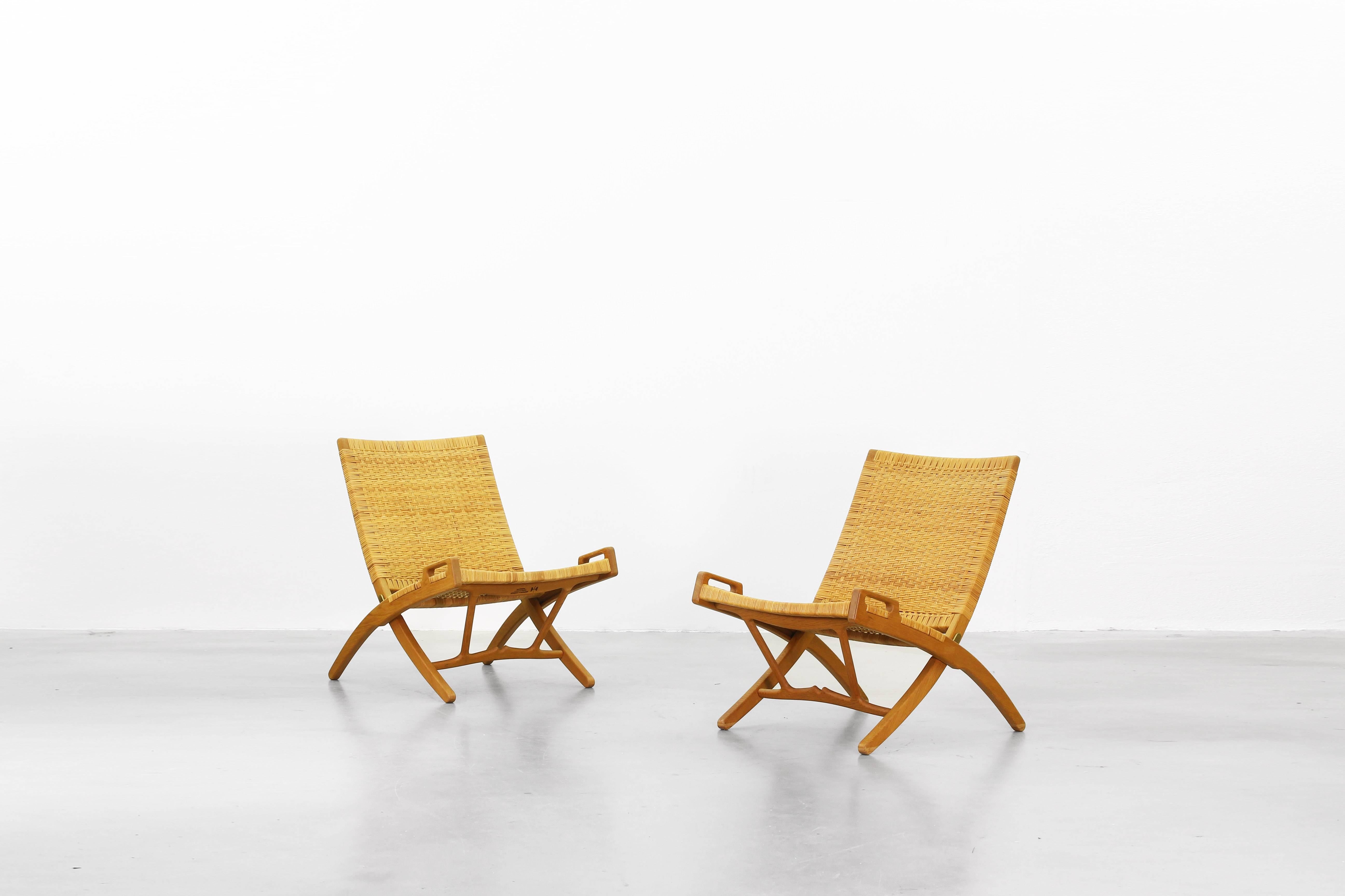 A beautiful pair of folding lounge chairs designed by Hans J. Wegner for Johannes Hansen in 1949. These beautiful pieces are made of oak and cane and both lounge chairs are in an excellent original condition without any marks or cracks.