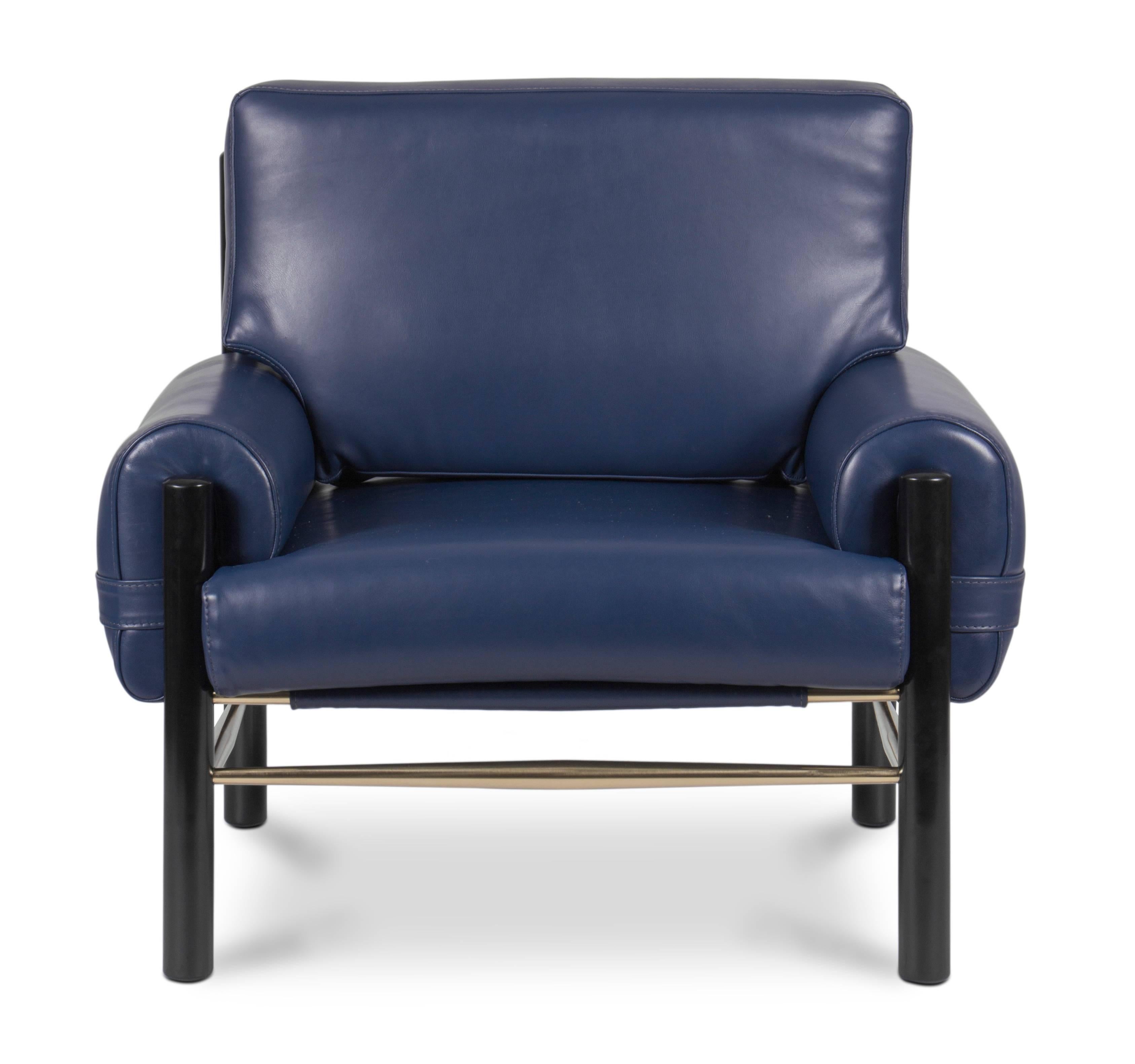 Inspired by Midcentury design, this leather upholstery armchair has a slender yet boxy structure. The boxy look is due to the frame of the chair although its details in polished brass give it a lighter touch. The combination of this material and the