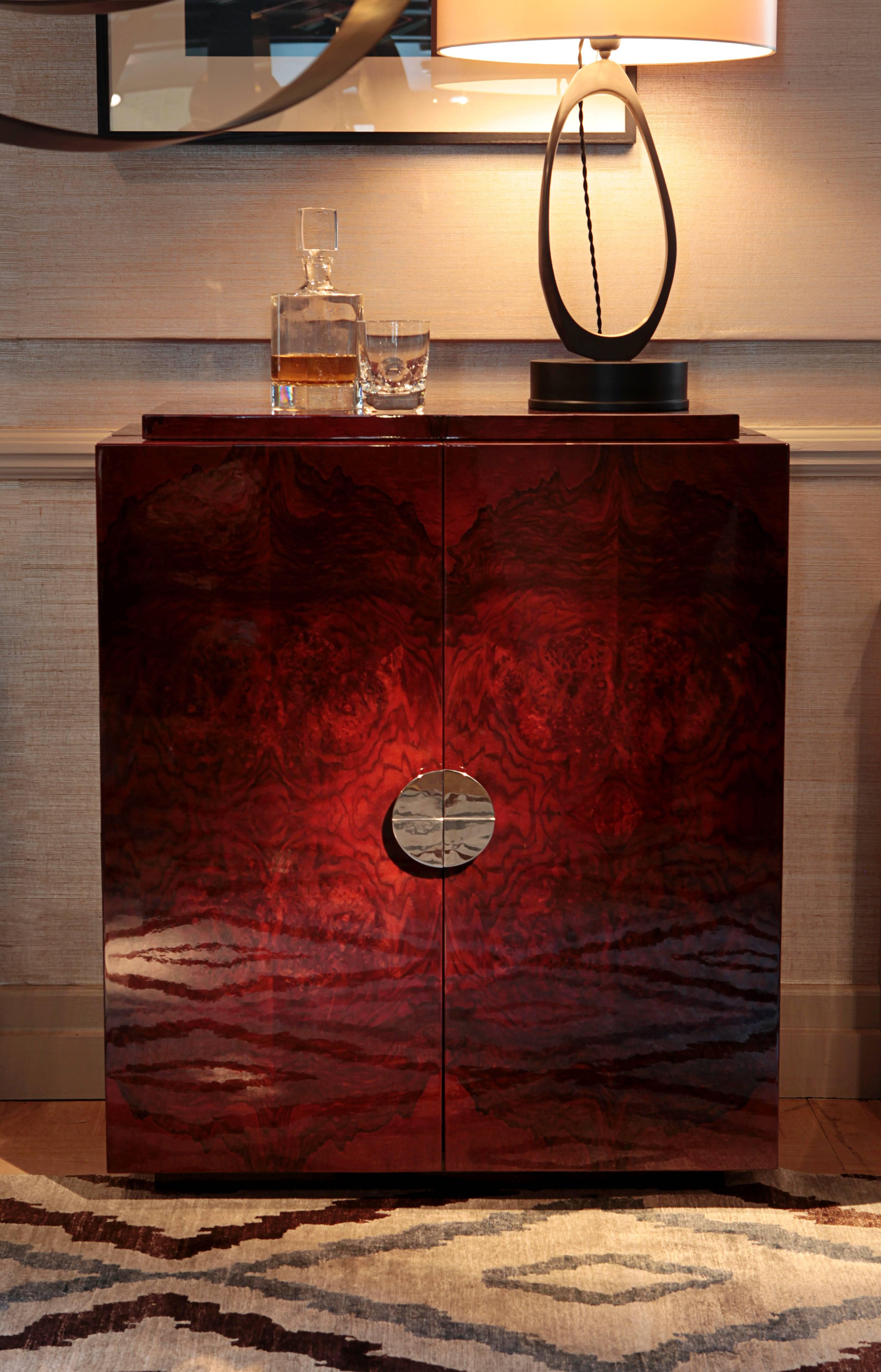 Designed by Simon Stewart for Charles Burnand. The Deco inspired, Bond Drinks cabinet is made from stained walnut burr veneer high gloss lacquer exterior with high gloss maple, mirror interior with glass shelves inside the doors. 
The cabinet sits
