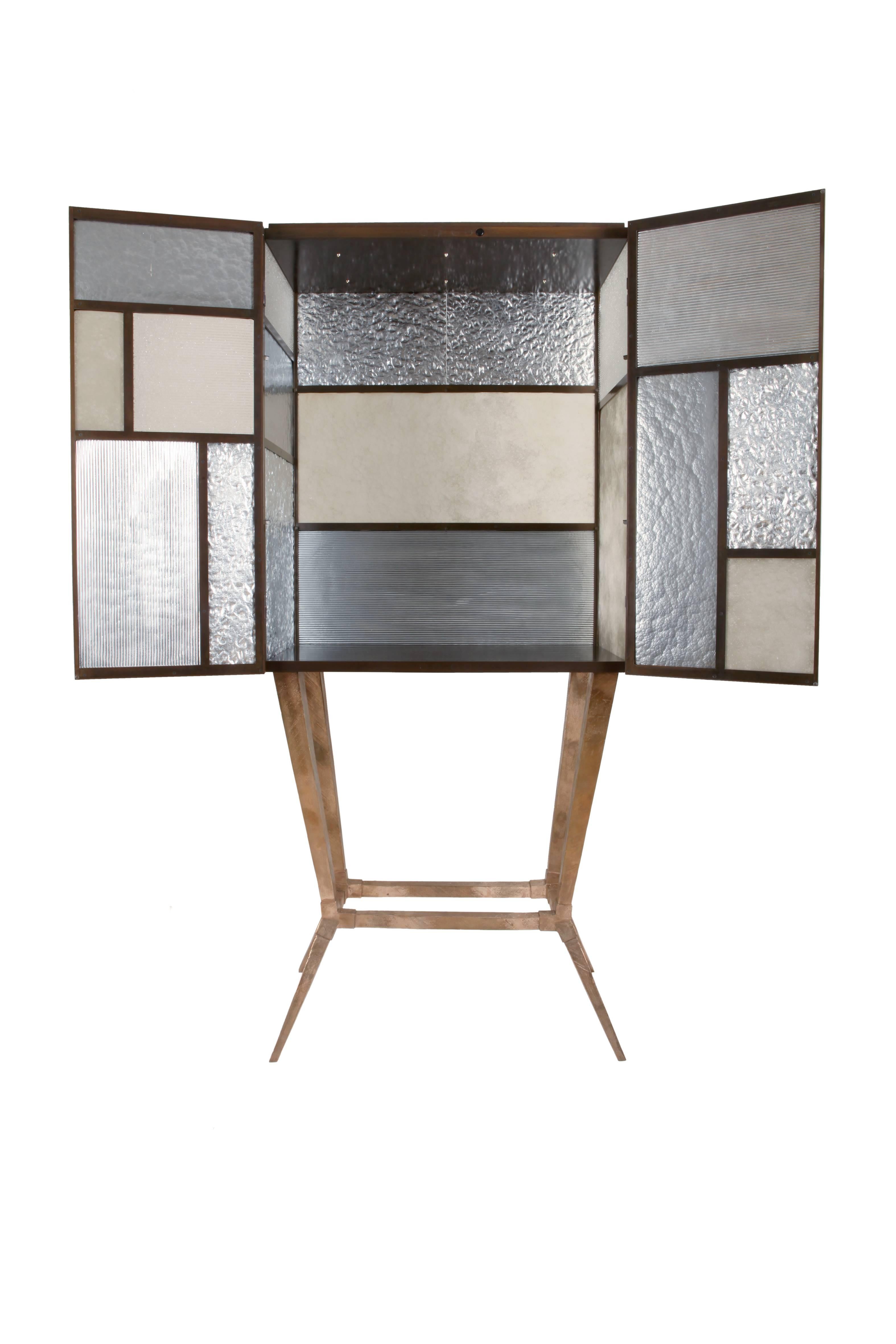 The tableau drinks cabinet is formed from 17 individually hand floated pieces of Murano glass, set in a patinated steel frame on top of a cast bronze base in it's natural form.
The doors are held in place with hidden magnets, and the inside of the