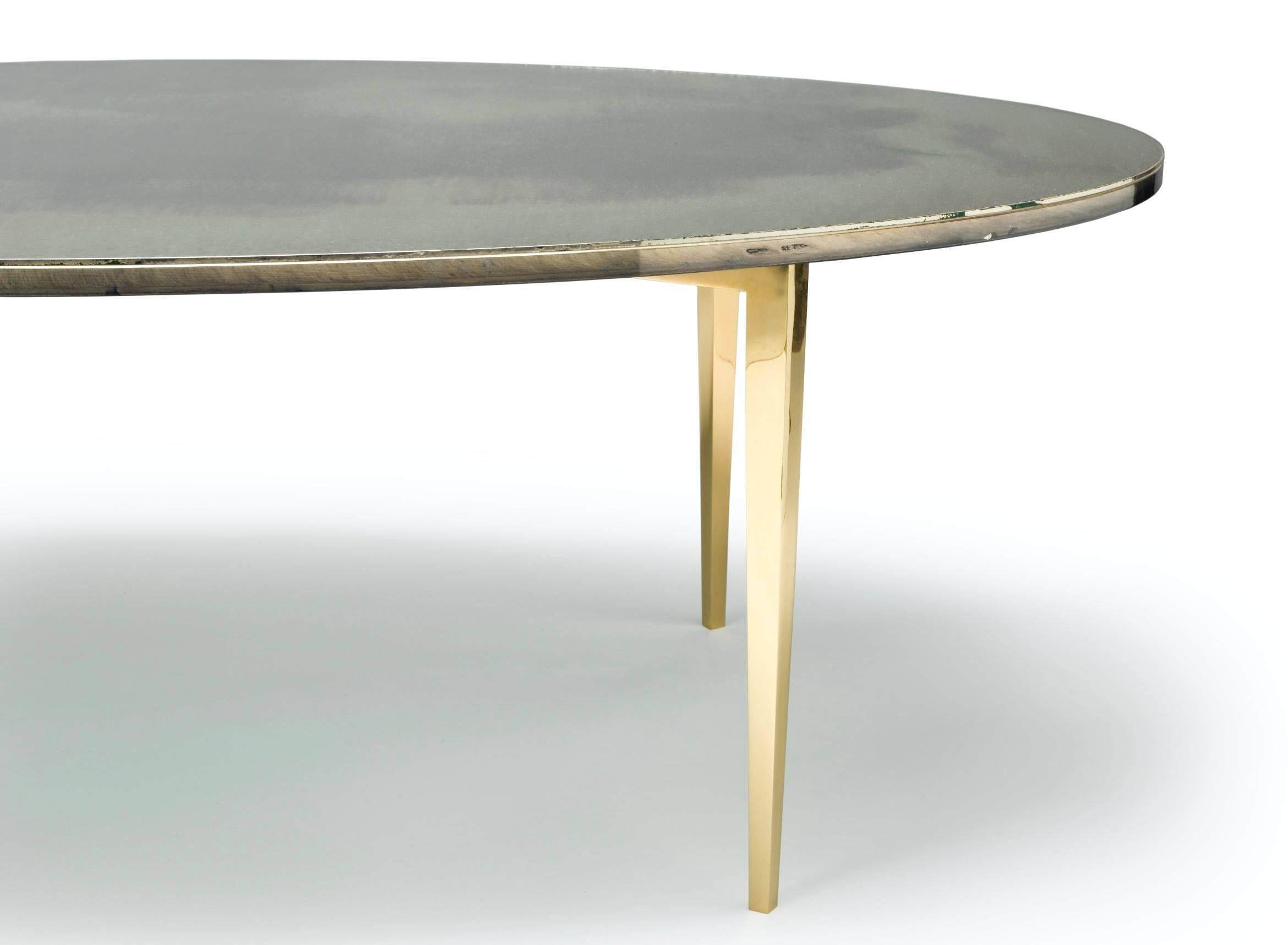 Oval cocktail table on brass base with gold slip and hand-silvered glass top using precious metals, gold, silver, bronze and iron.

Protected with a glass coverslip.