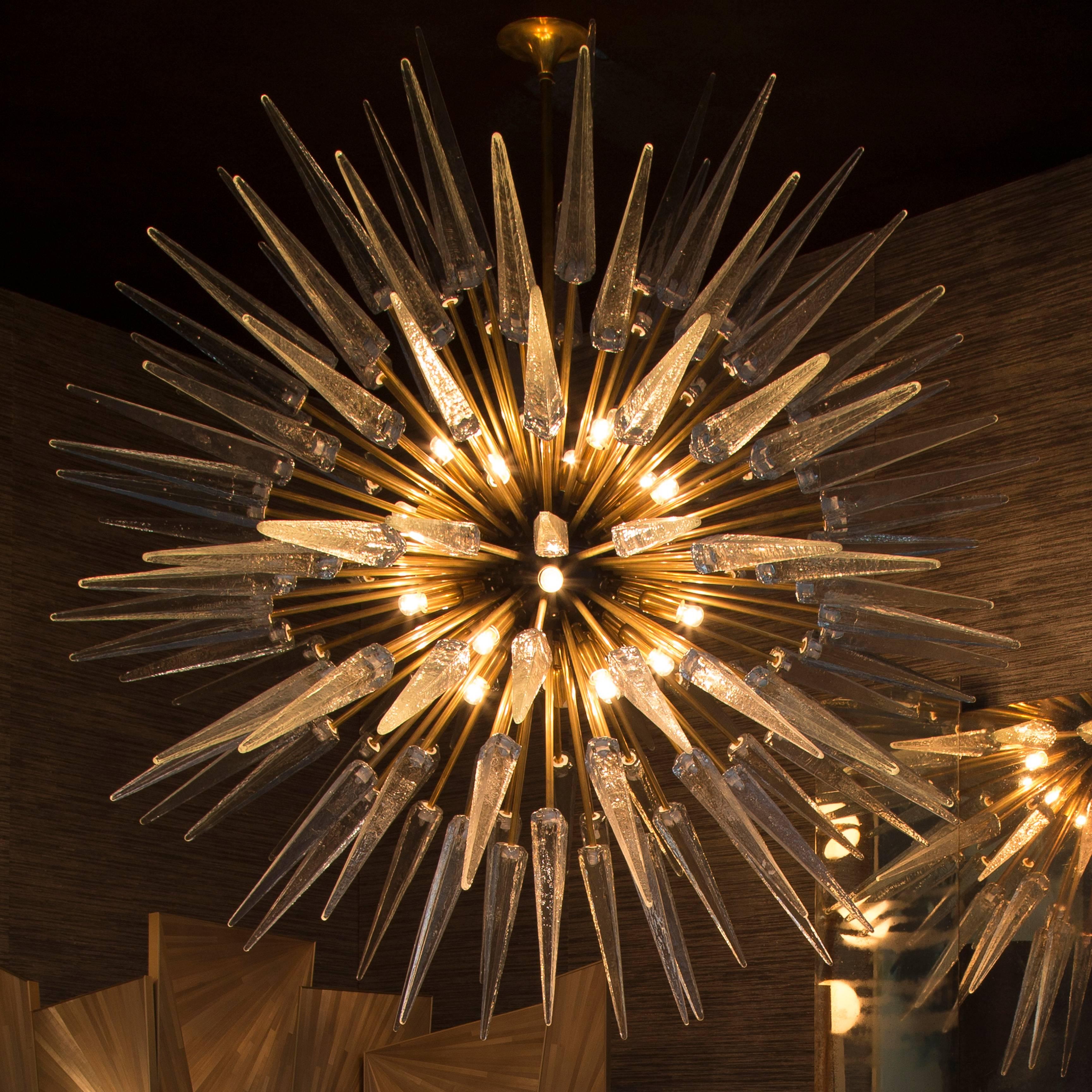 Sputnik shard chandelier comprising of 127 Murano glass shards with on natural, un-lacquered brass rods of two lengths fixed to a central black orb.
Light bulbs are fixed to the central orb, giving a central glow of light.

Takes SES bulbs. Wired