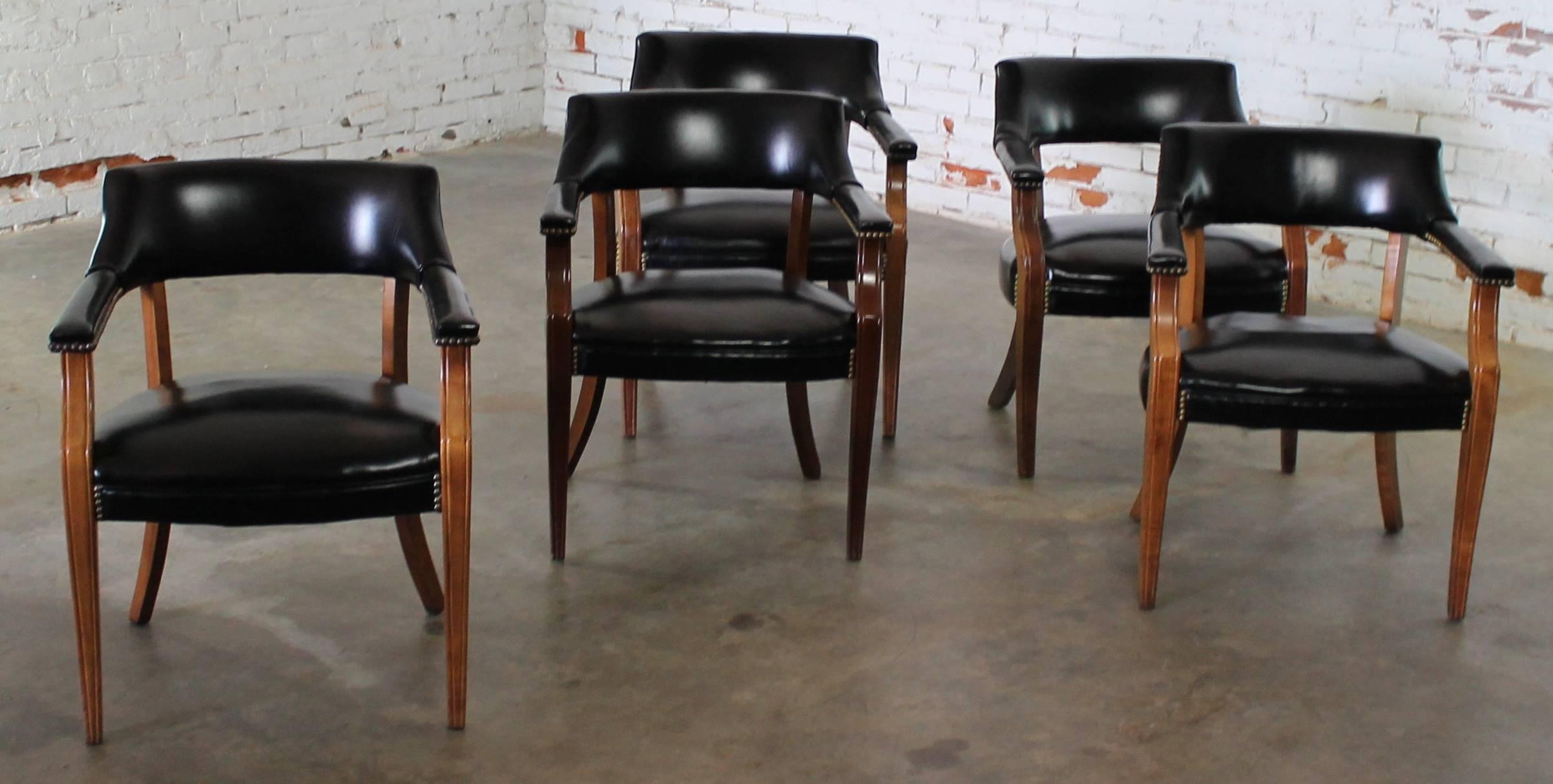 Handsome set of five solid walnut captain chairs with black faux leather upholstery and nailhead detail. Perfect used with a round table for card games or dining.

This set of five vintage captain chairs are in extremely great shape. They are