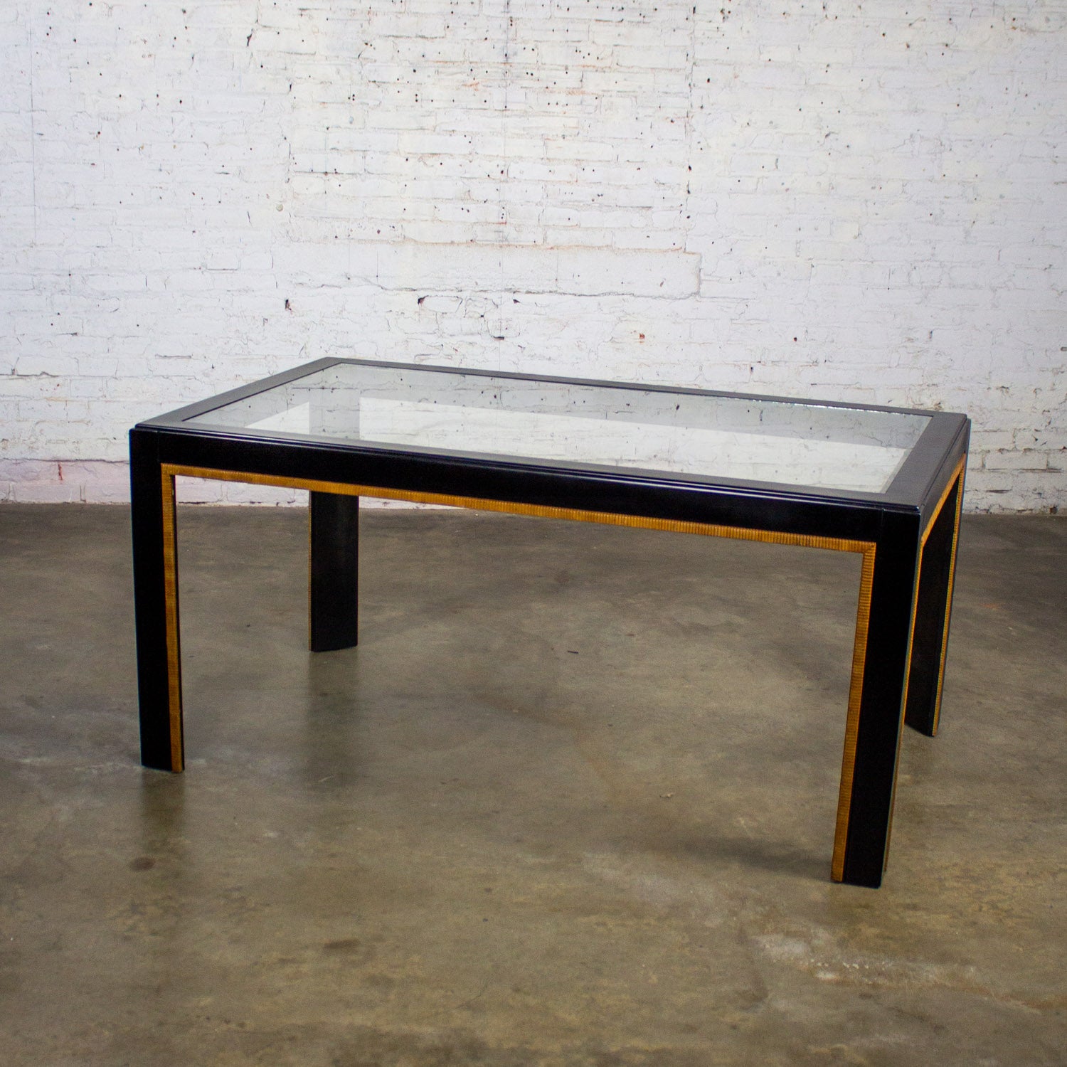 Gorgeous Late 20th Century Modern Campaign Parsons style dining table with black painted rectangular frame, faux rattan trimmed edges, and rectangular clear glass inset. Beautiful condition, keeping in mind that this is vintage and not new so will
