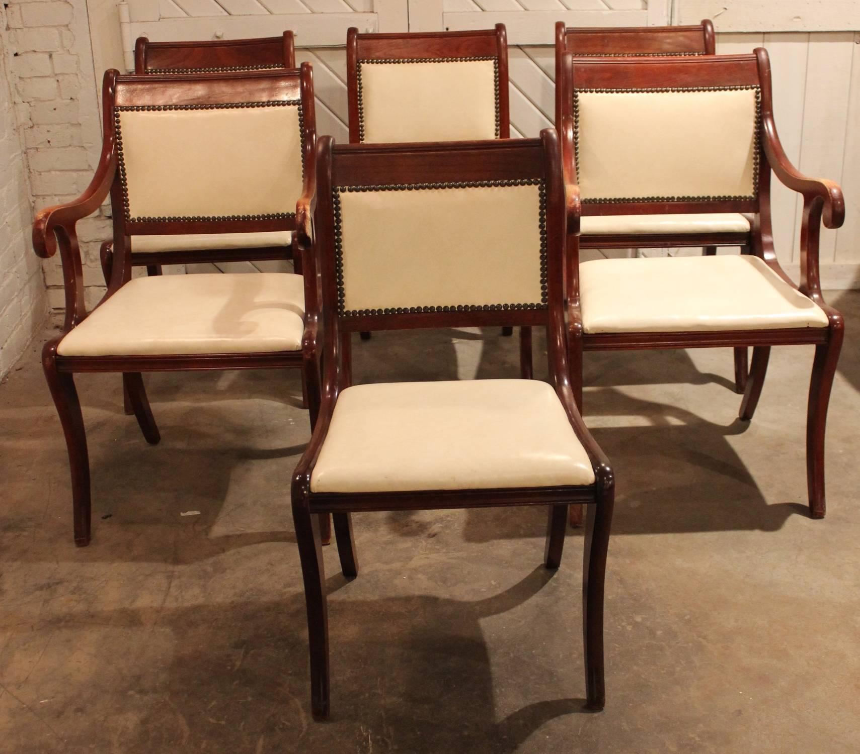 Fabulous set of six Regency style dining chairs in mahogany with white faux leather upholstery. Two arm chairs for the host and Hostess and four armless chairs. The upholstery is in excellent condition and the wood has a wonderful vintage age