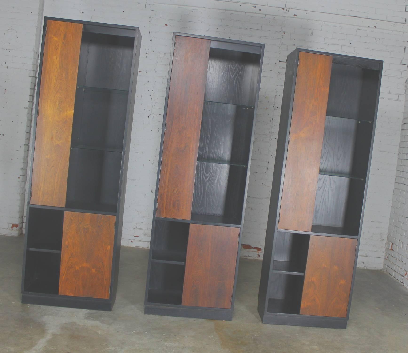 Outstanding set of three rosewood and ebonized oak alternating door display cabinets lighted with glass shelves attributed to Harvey Probber, circa 1960 and in wonderful vintage condition; however, please see long description for details. This is