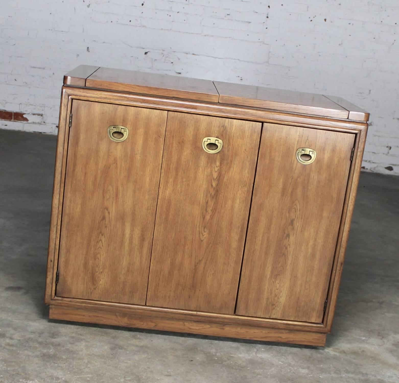 Very handsome dry bar in Mid-Century Campaign style done in oak or ash by Drexel Heritage Furniture for their passage line. This rolling bar cabinet is in phenomenal, circa 1970 condition.

Everyone needs a rolling dry bar now! It is so Mad Men.