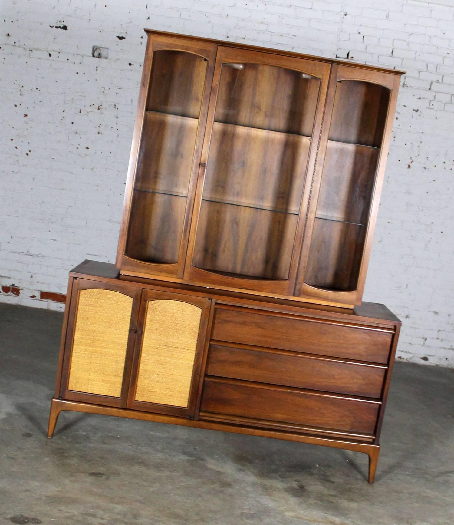Handsome Mid-Century Modern lighted china display cabinet in two pieces from the Rhythm Collection by Lane. The doors are reversible from cane to walnut. This cabinet is in very fine vintage condition and circa 1960.

This cabinet is one of the