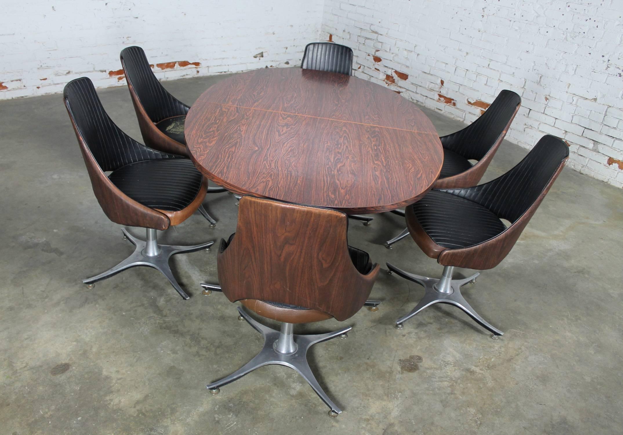 Fun and funky Mid-Century Modern dinette set featuring an oval table with double pedestal base of aluminum and six two toned wood grained and black vinyl swivel chairs with aluminum bases. In good vintage condition.
OK. I give up. I can’t find the