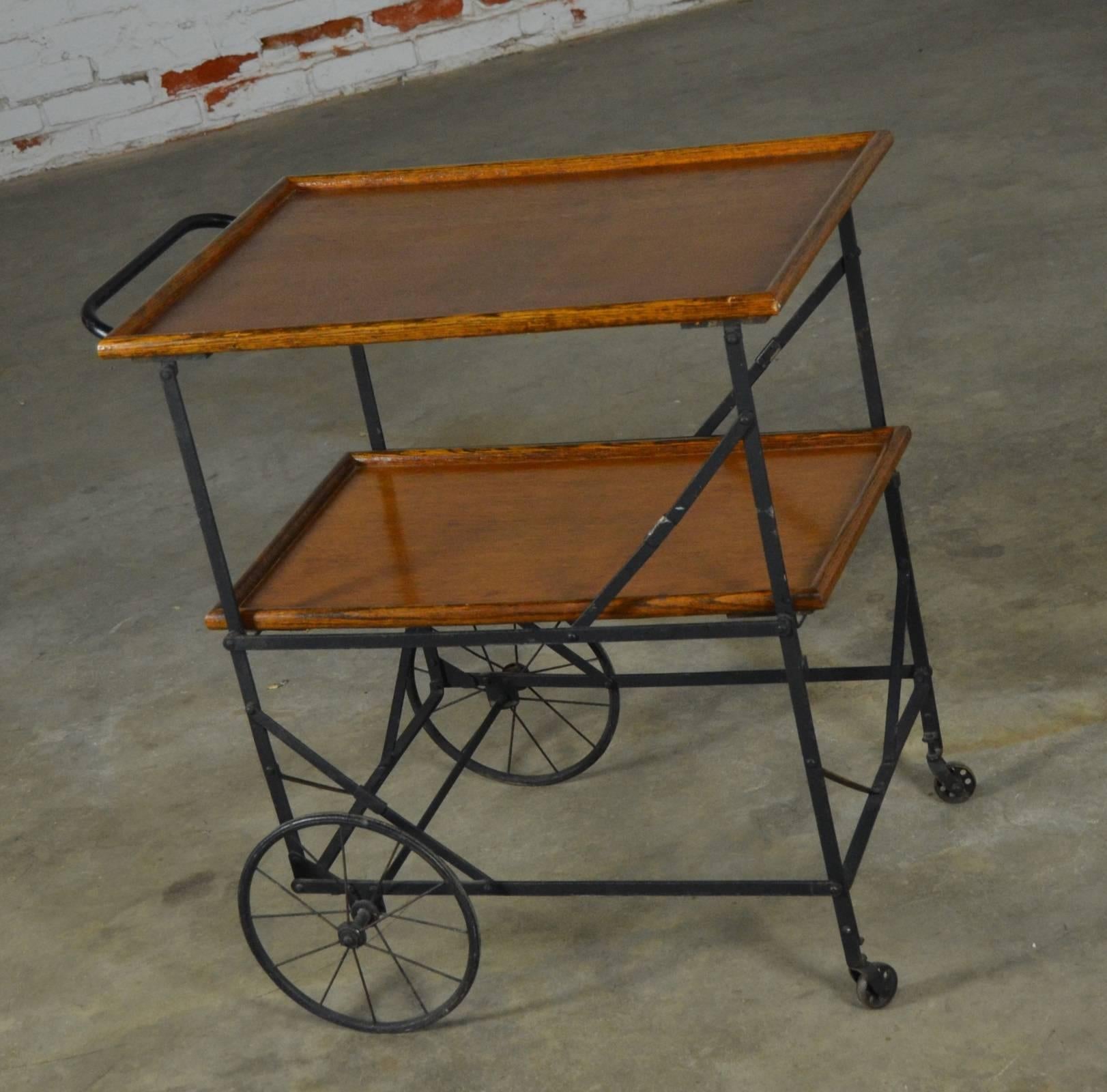 Fabulous Industrial chic antique rolling and folding tea cart, bar cart, or hotel serving trolley consisting of black painted iron with oak shelves and spooked baby buggy style wheels. In wonderful antique condition.

Presenting this incredible