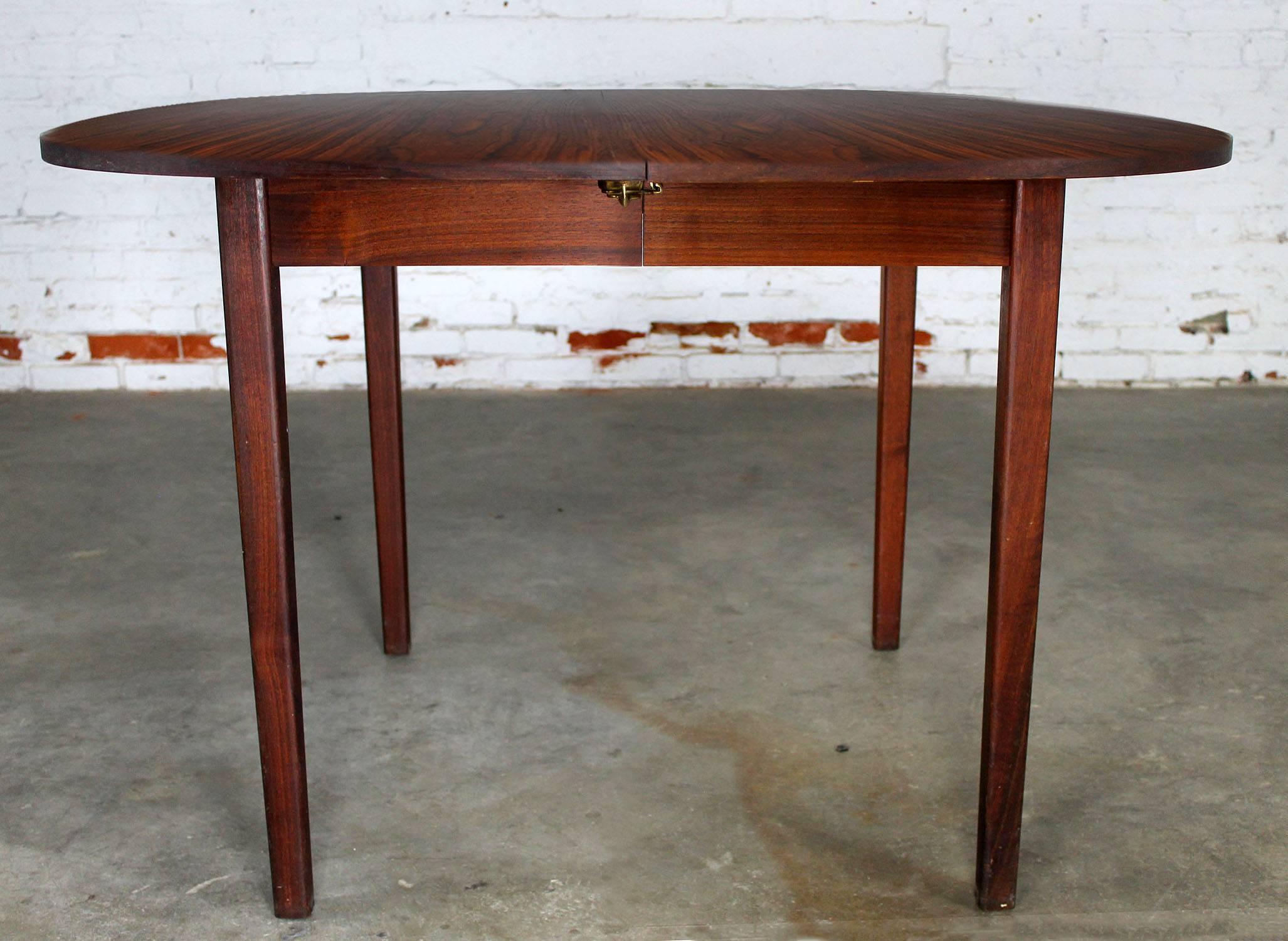 Handsome expanding Mid-Century Modern rosewood dining table. Starts out with no leaves as a squircle and with the addition of one or two leaves becomes an oval. In wonderful vintage condition with the normal small nicks and dings for its circa 1960s