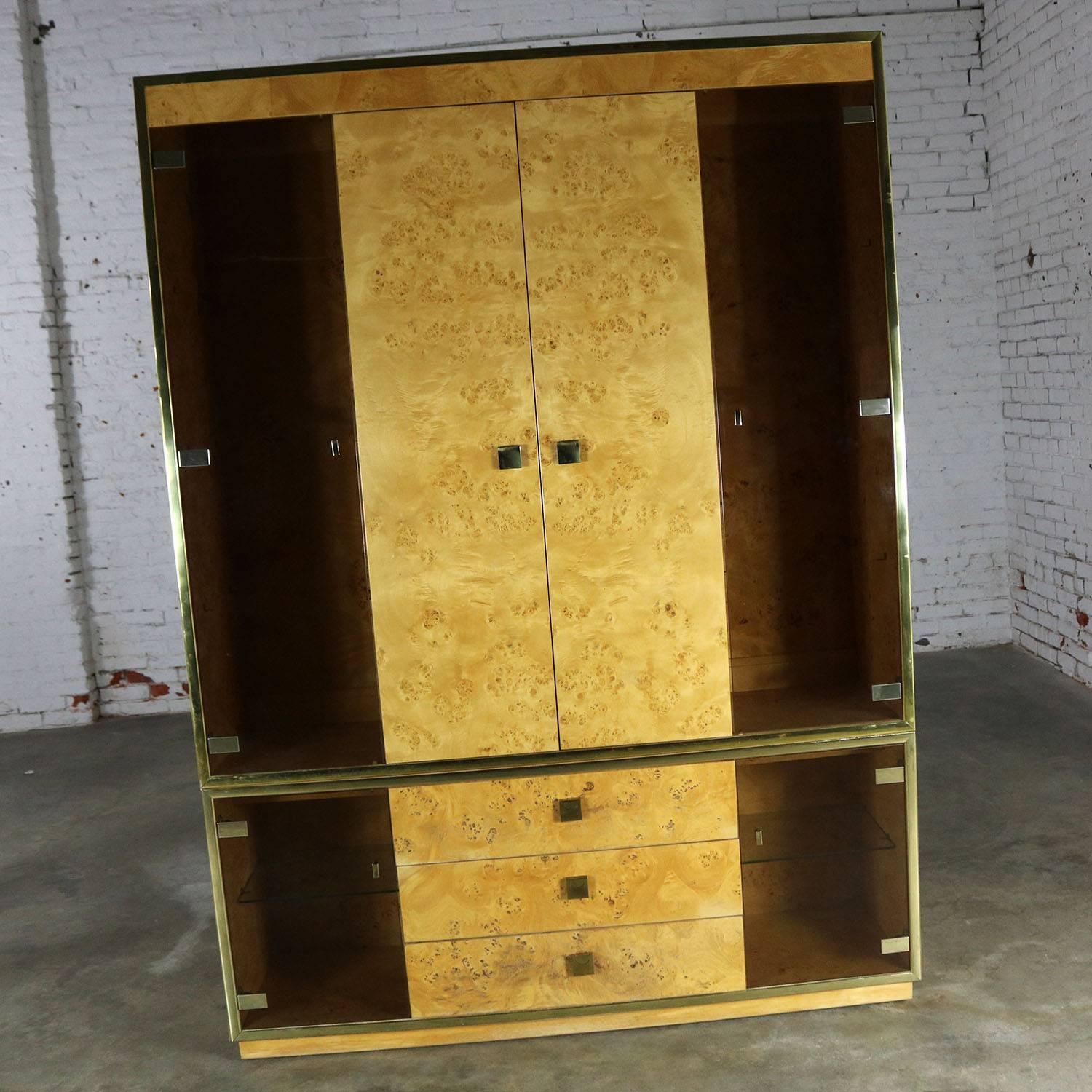 Handsome wall unit lighted display cabinet in a light burled wood veneer and smoked glass doors with brass trim and handles by Founders Furniture. This piece is in good vintage condition. It does have some dings and small flaws as you would expect