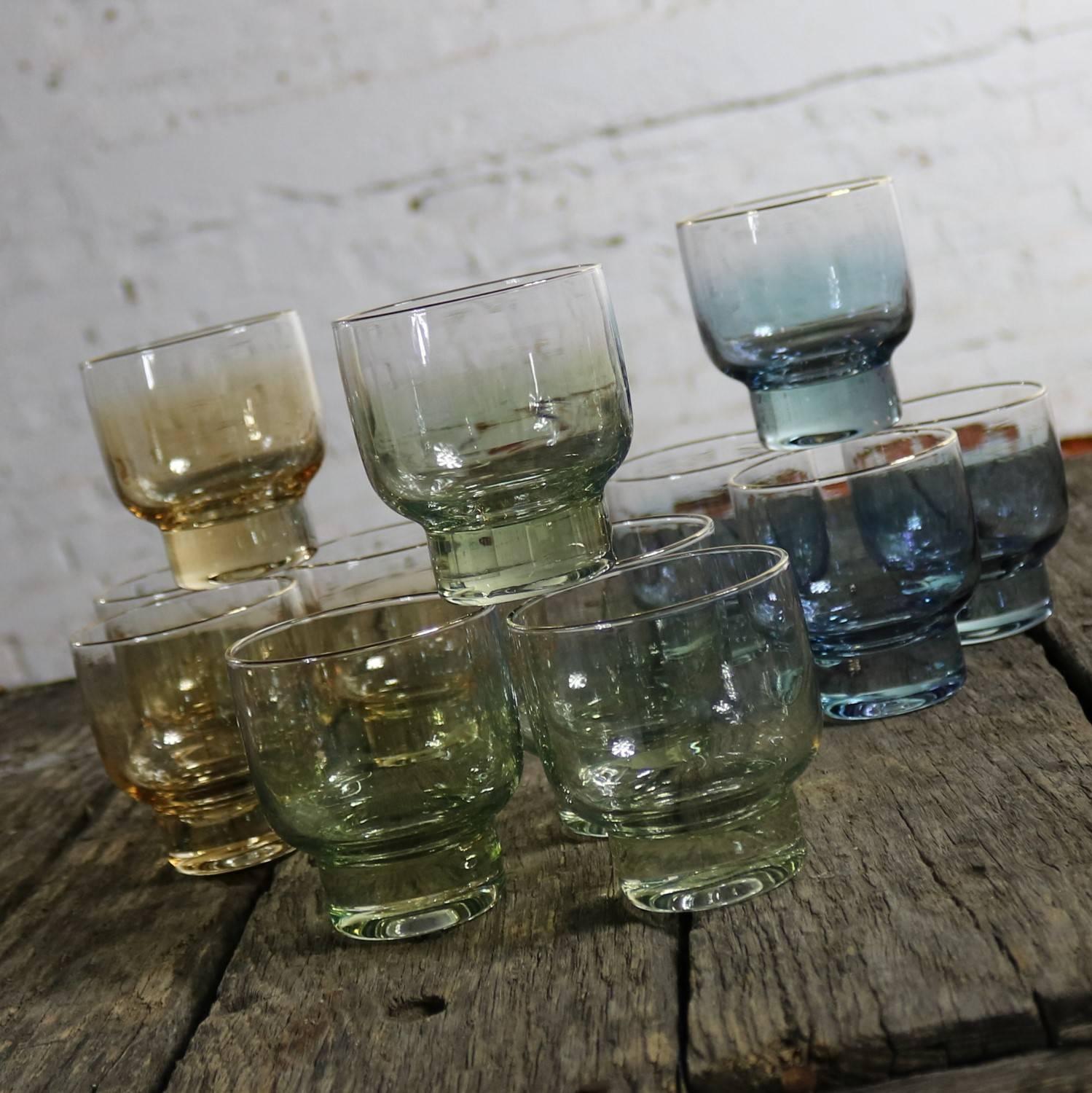 Fabulous set of 12 Mid-Century Modern footed cocktail glasses. Four sapphire blue ombre, four emerald green ombre, and four topaz yellow ombre with gold rim. All are in excellent condition apart from two of the sapphire which have some of the gold