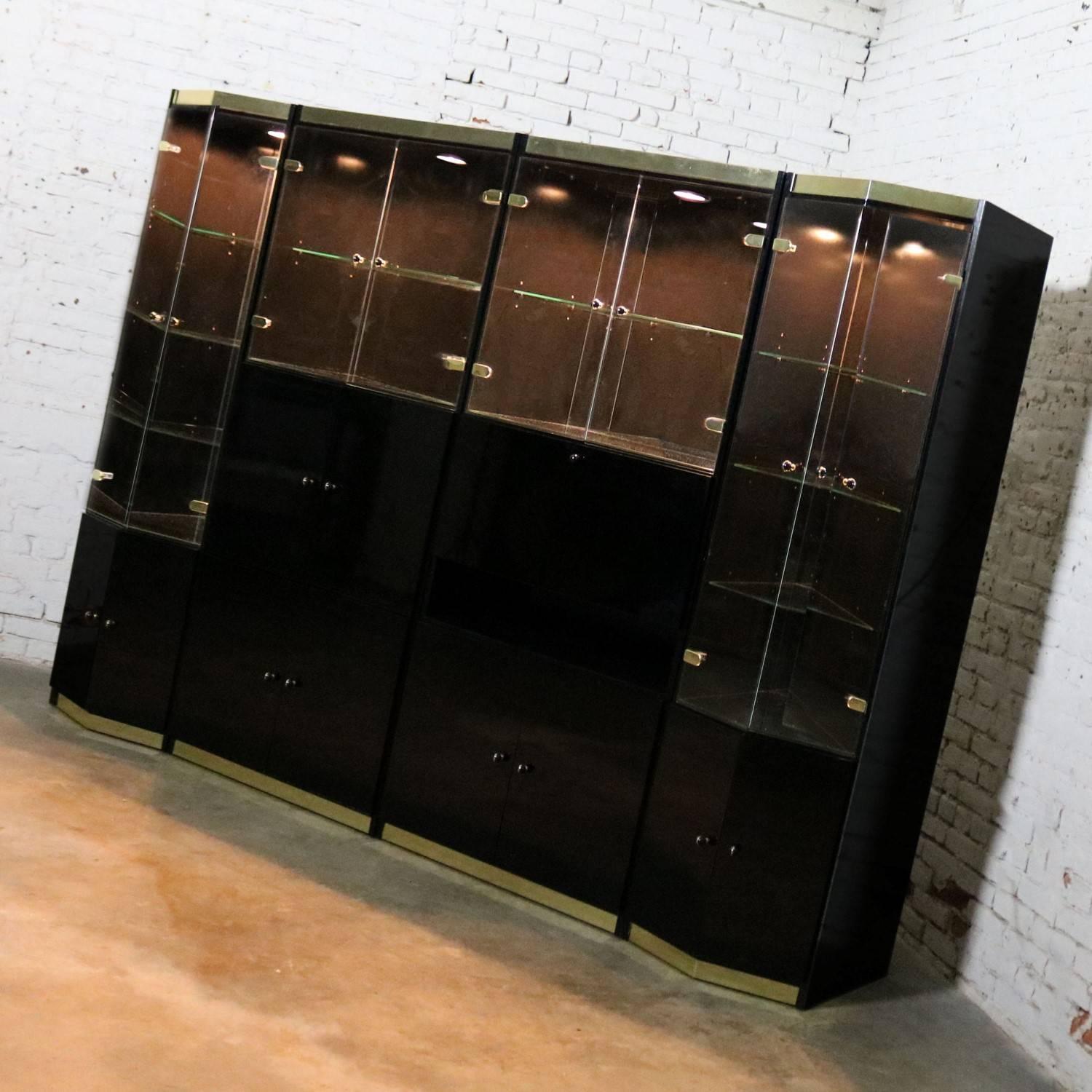 Impressive Italian four-piece modular freestanding wall unit bookcase display cabinet in black laminate with glass doors and brass accents. It even has a drop-down desk. It is in wonderful vintage condition apart from a top corner chip in one of the