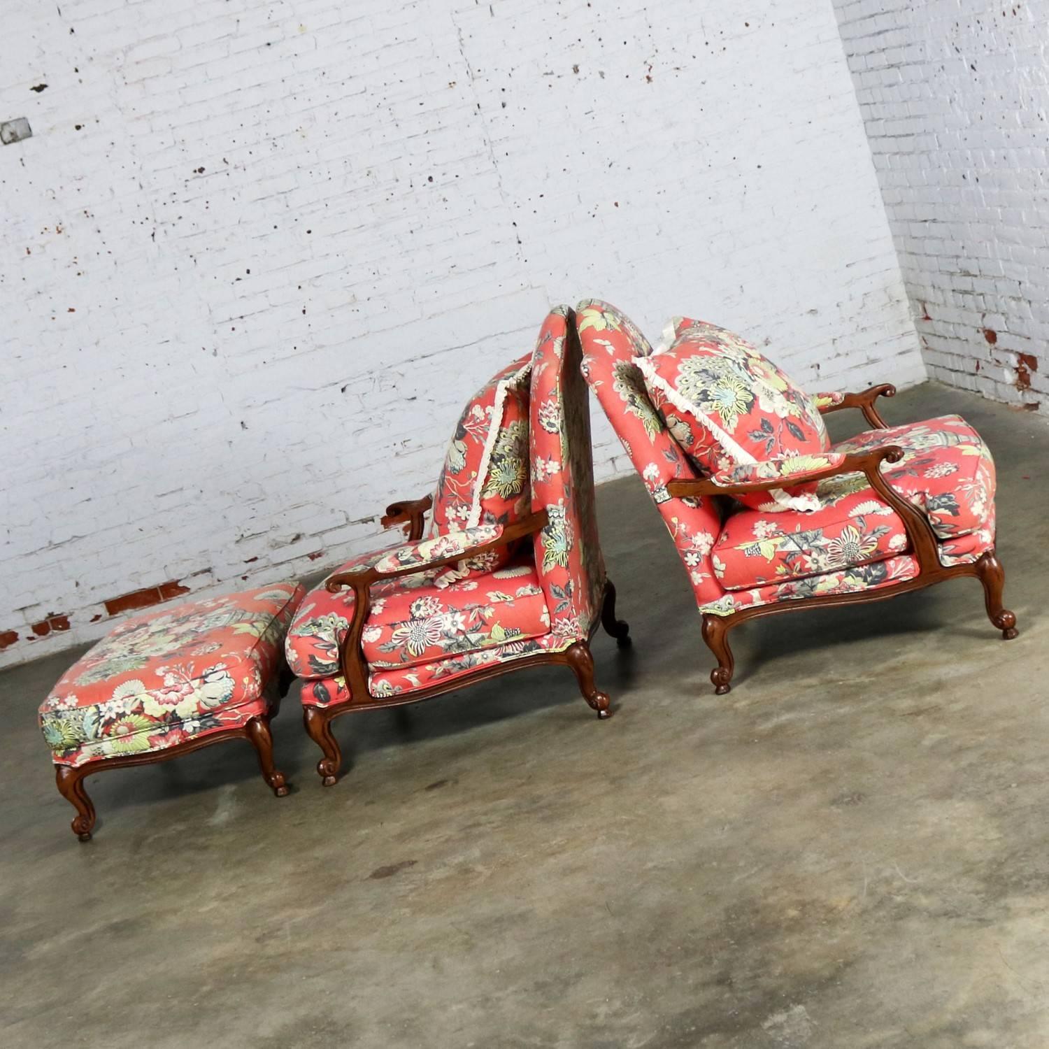 Great pair of very overscale fauteuil chairs with a shared ottoman by C.R. Laine in a coral or faded red floral cotton-like fabric. They are in wonderful pre-owned condition with a purposeful faded look; however the ottoman has a more faded look