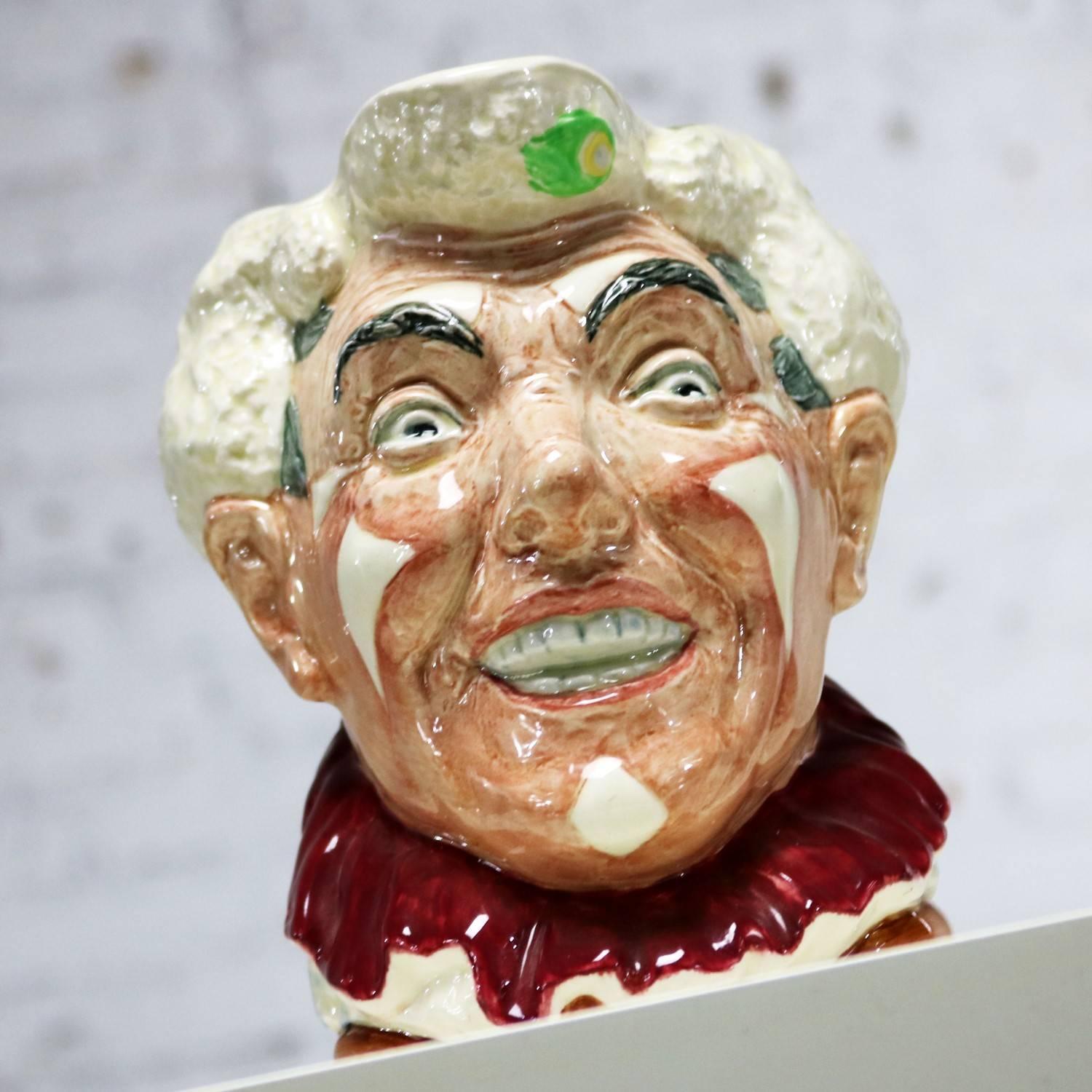 Magnifique pichet de personnage Royal Doulton alias toby jug le clown D6322 avec des cheveux blancs et un collier à volants rouges. Il est en fabuleux état vintage, sans éclats, fissures, ou chiggers que nous avons trouvé, circa 1951-1955.

Les