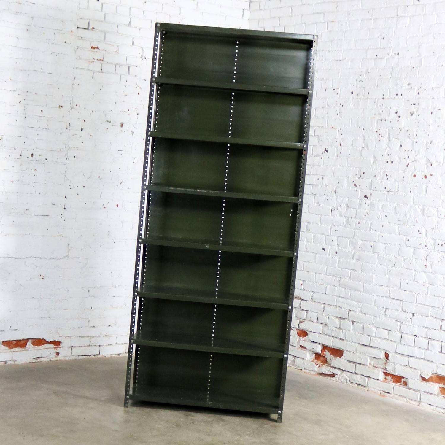 Wonderful Industrial steel bookcase or shelving unit. It retains its original Army green paint but with awesome age patina. It is in solid sturdy condition but has age and use dings, dents, scratches, and bare spots that creates a fabulous age