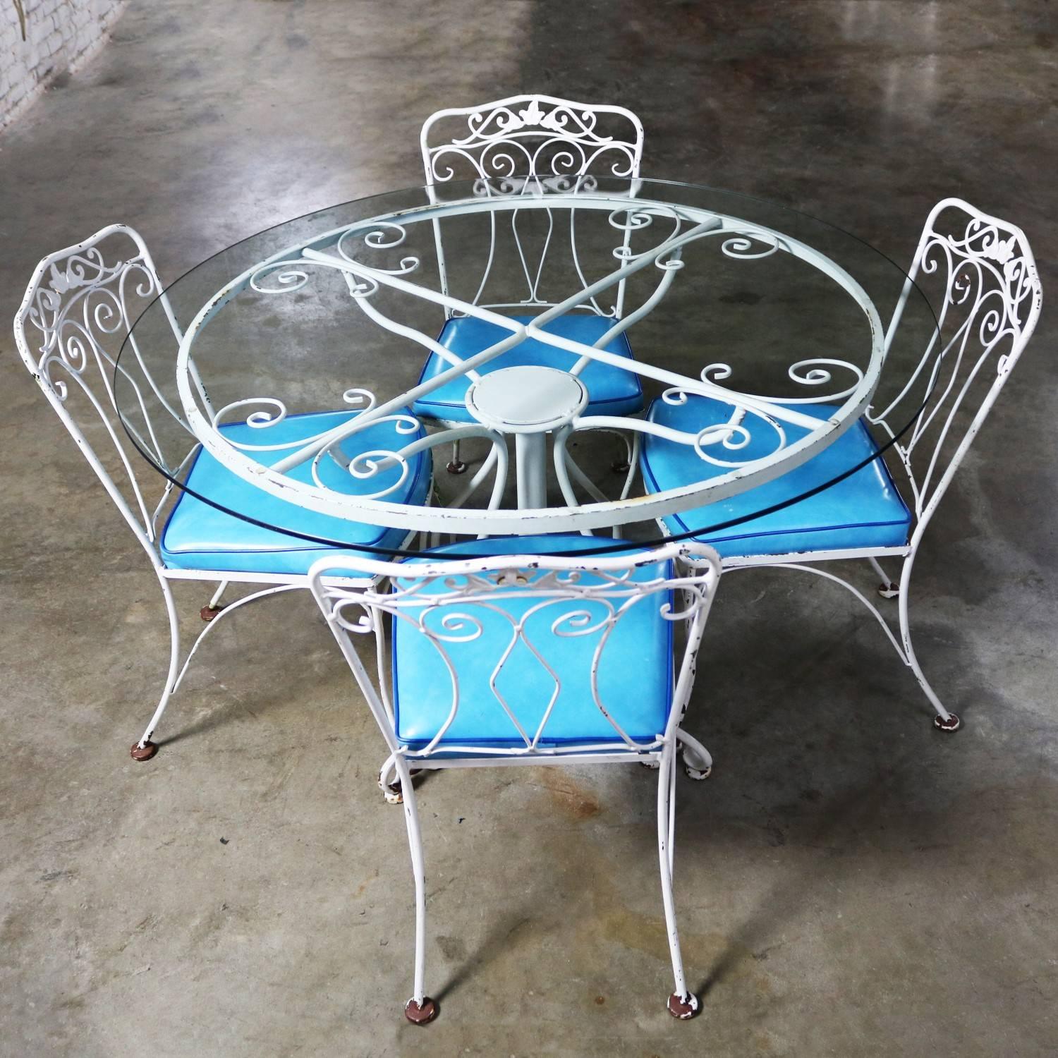 Lovely Salterini style wrought iron patio set consisting of a round dining table with pedestal base and glass top and four chairs with turquoise vinyl attached seats. This circa 1950s set is in wonderful vintage condition. The white paint on the
