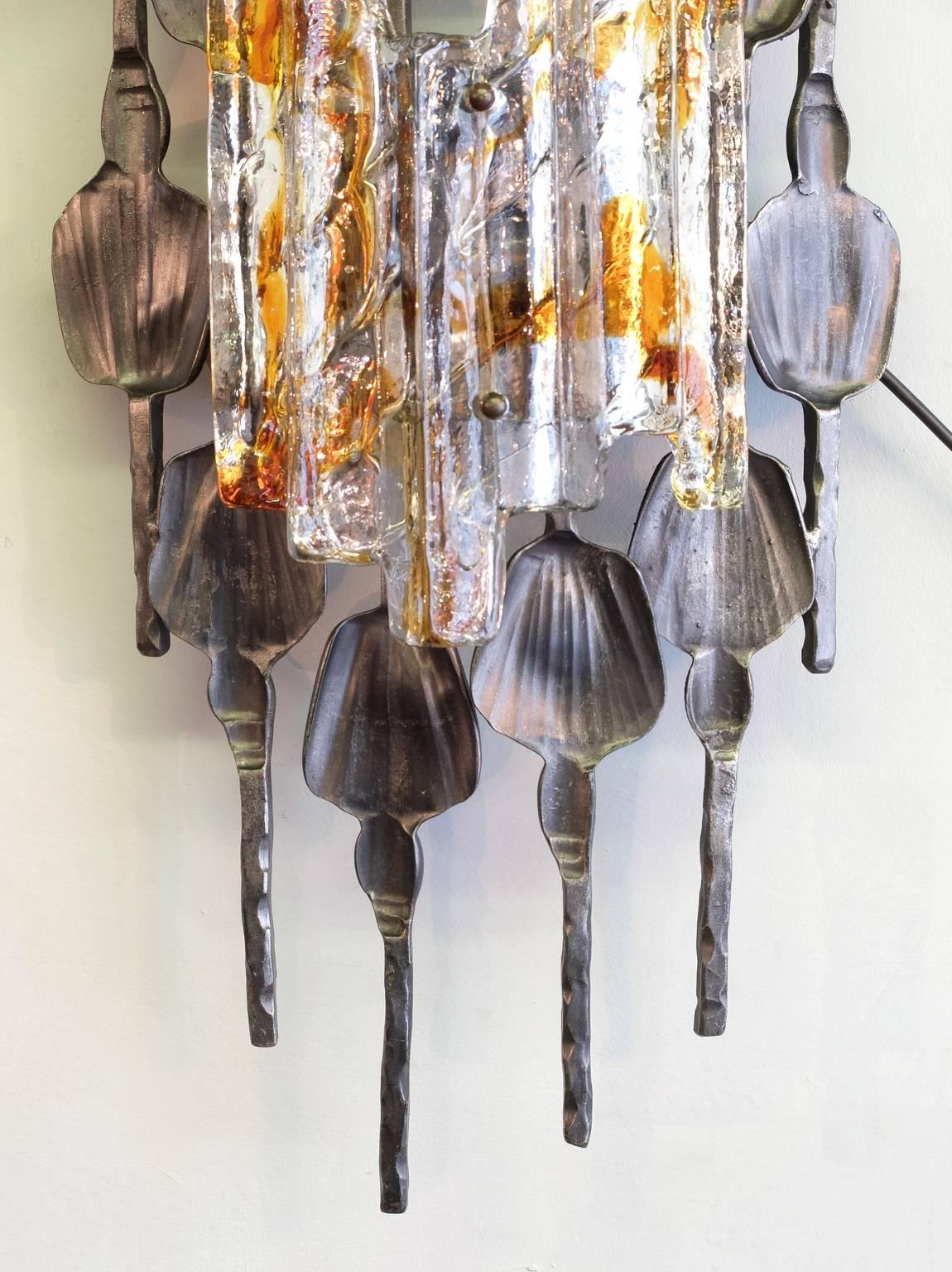 A large wall sconce from Swedish design company A & E Design, circa 1970, in the Brutalist style. The hand-wrought iron surround has a good patination and is set off by the Murano ice glass with its clear and amber tones. This wall light has been