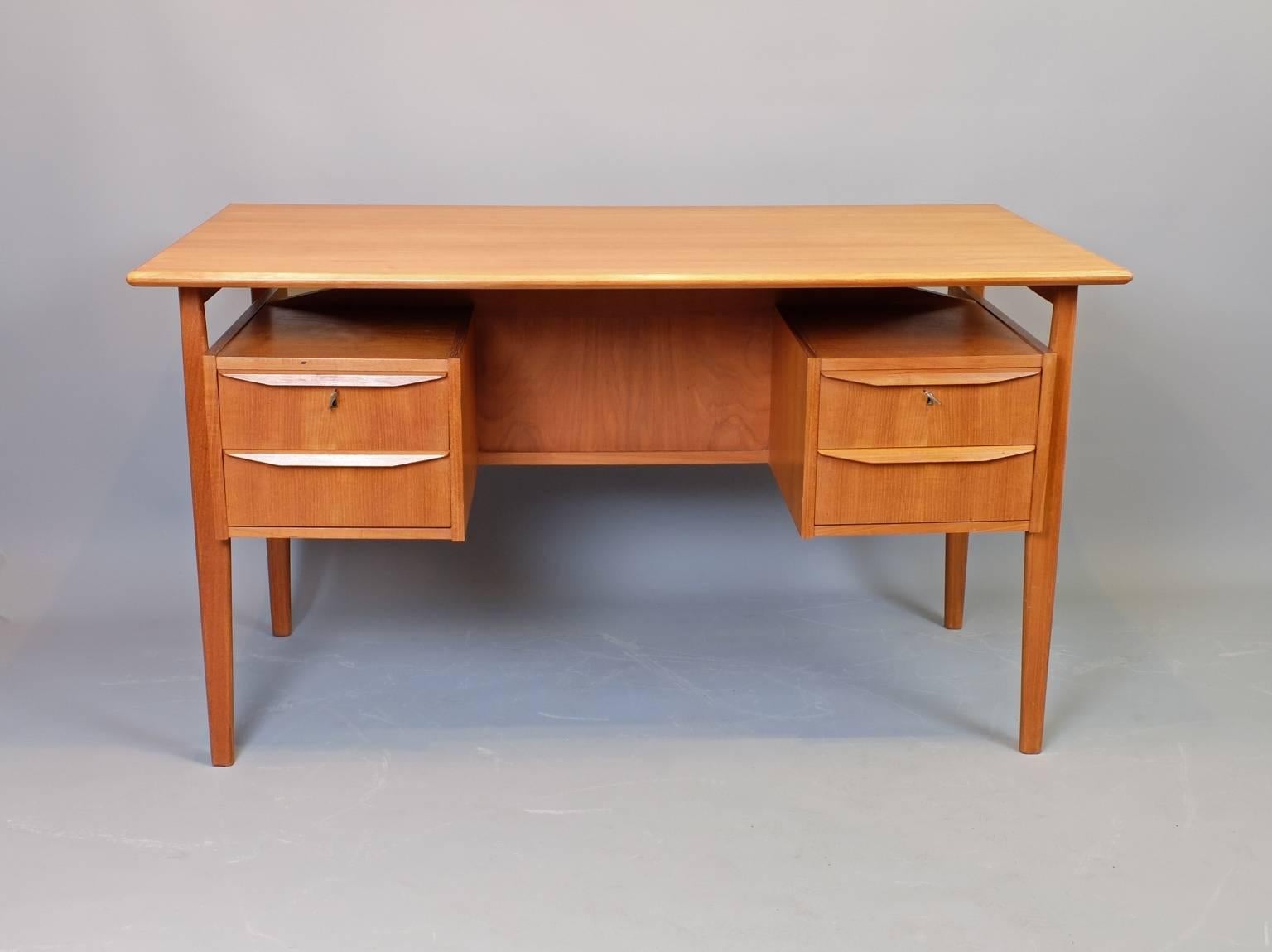 A golden teak floating top desk by G Tibergaard, Denmark, circa 1960. Two locking drawers with original and working keys. Features a useful and decorative bookshelf at the back. The kneehole opening measures 17.75