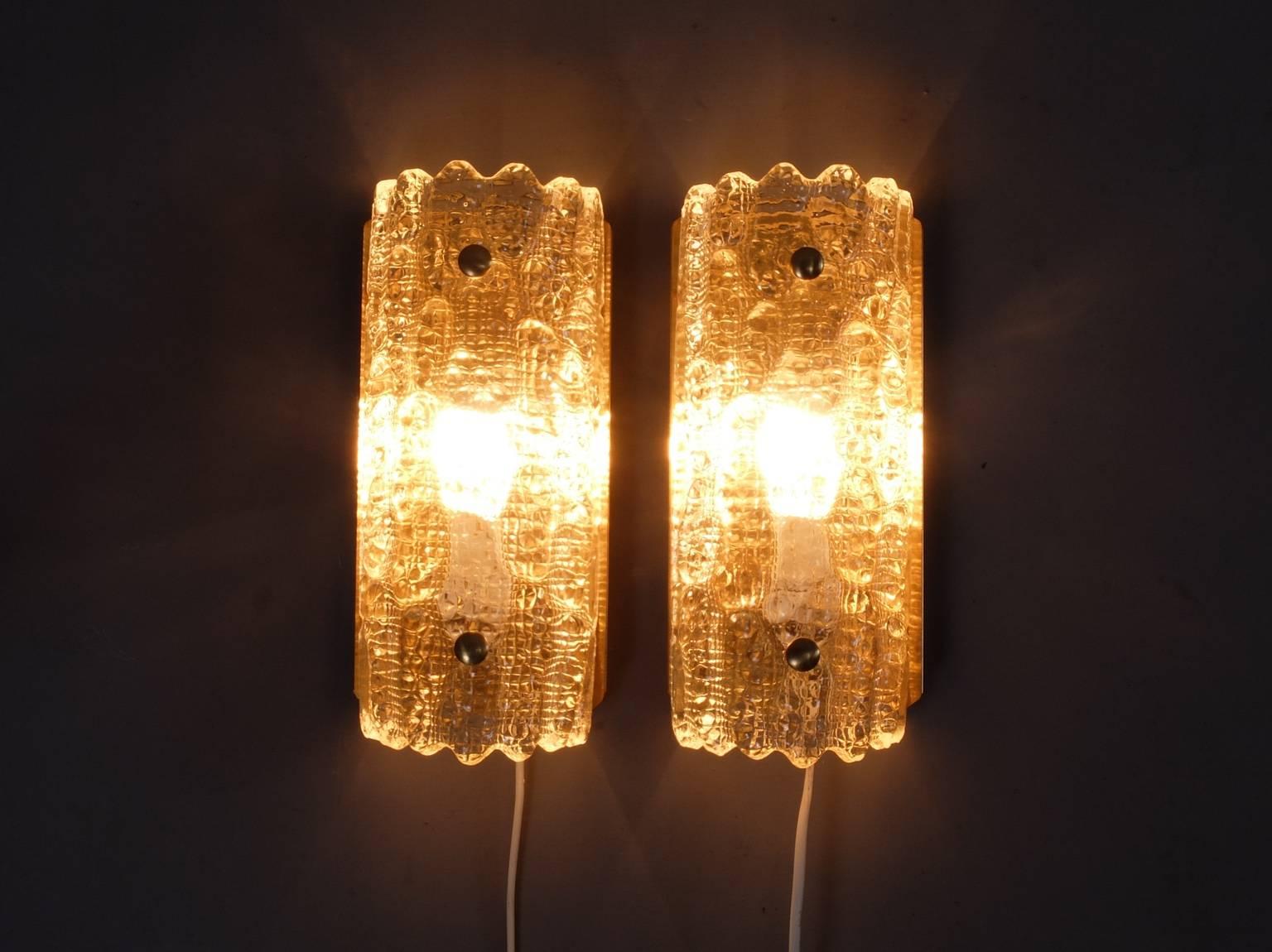 A pair of Carl Fagerlund Orrefors glass sconces produced by Lyfa in the 1960s. These wall lights feature curved and textured glass from Swedish glass company Orrefors and are designed by Carl Fagerlund. The manufacturer is Danish lighting specialist