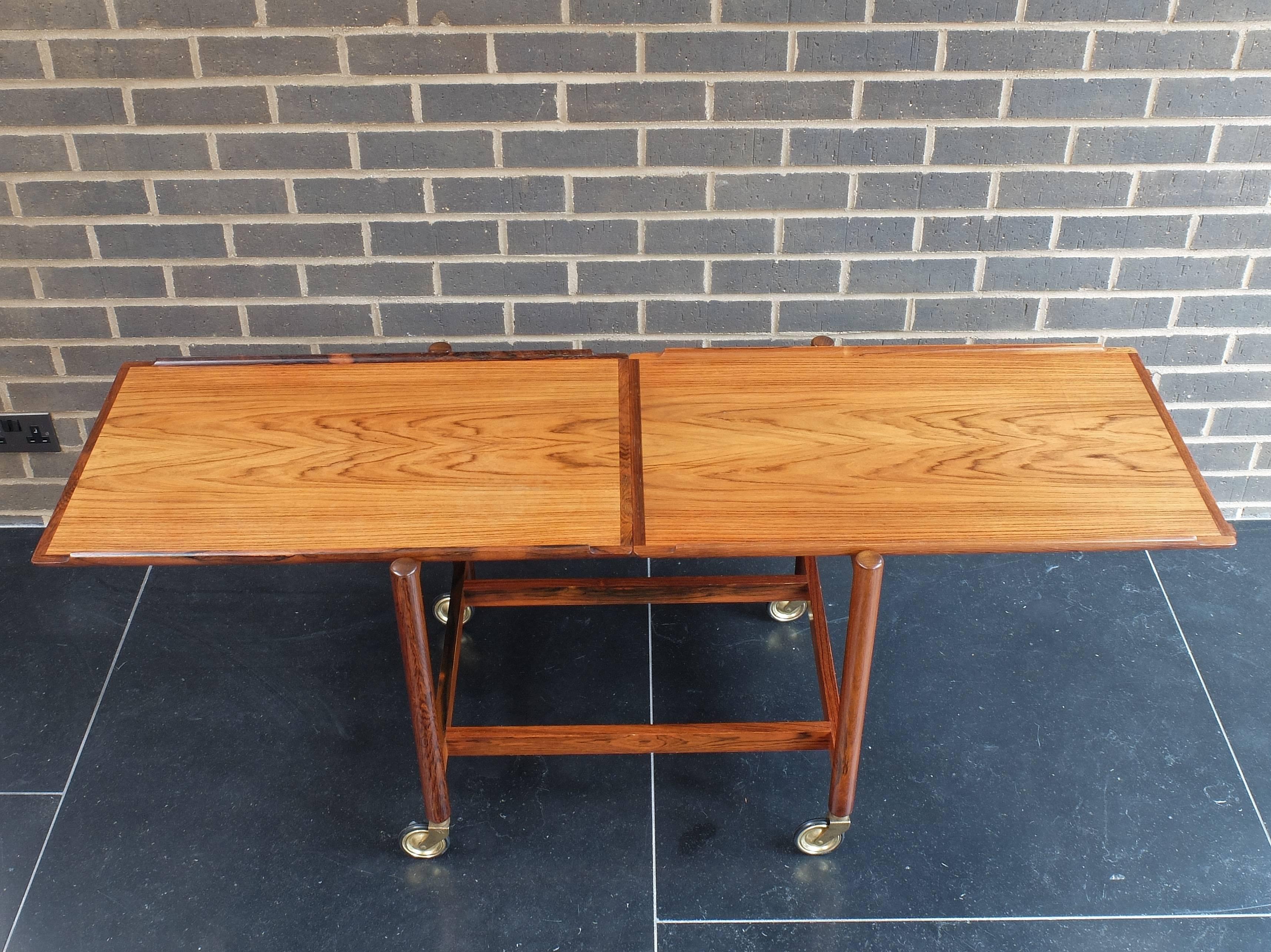 Designed by Poul Hundevad, Denmark, circa 1960. A useful tray topped tea trolley or bar cart in beautifully figured hardwood on brass and rubber wheels. The trays have beautifully rolled edges on two sides. The lower shelf can be removed and placed